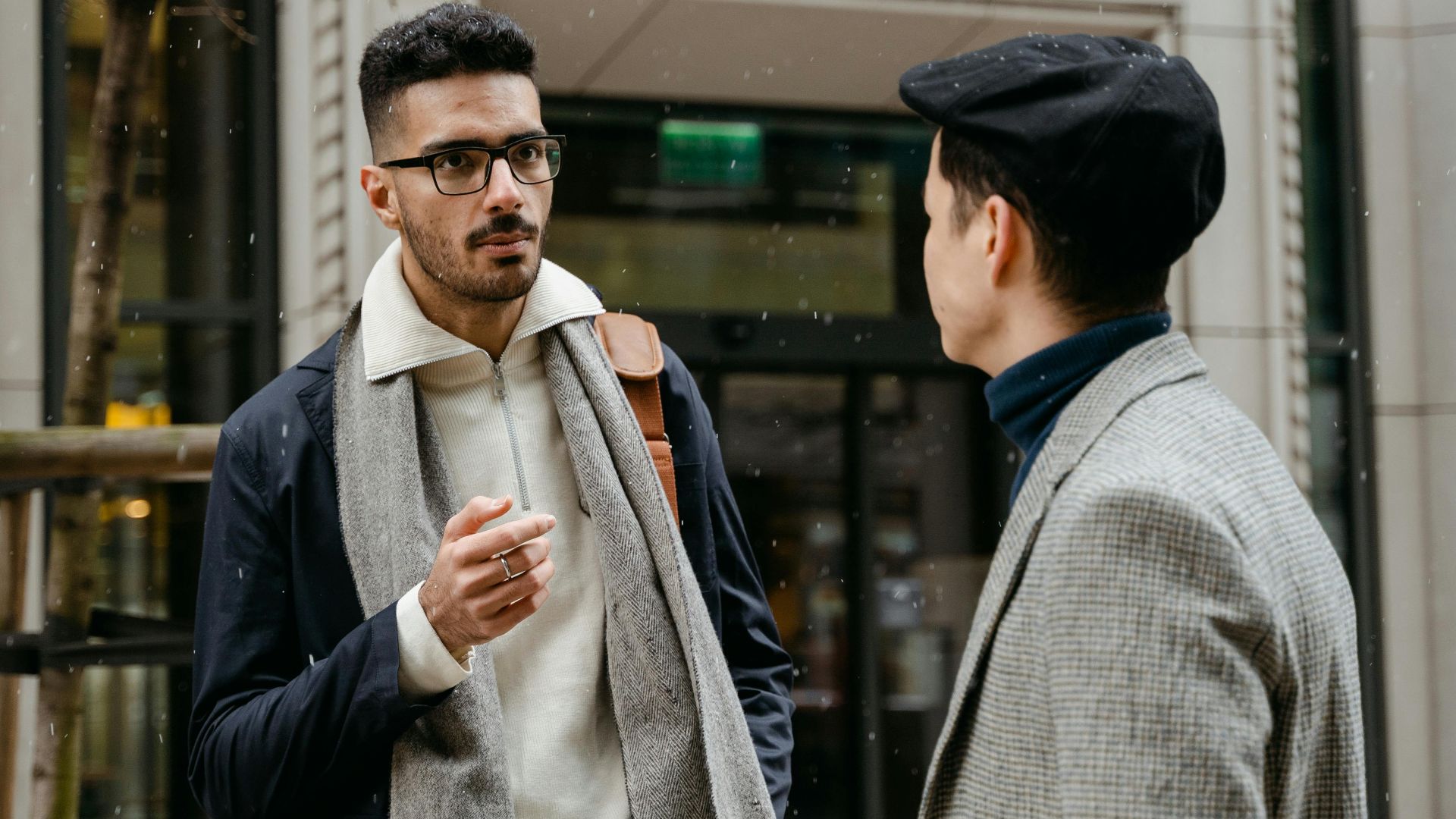 Two businessmen engaged in conversation outside in winter attire with snow falling lightly.