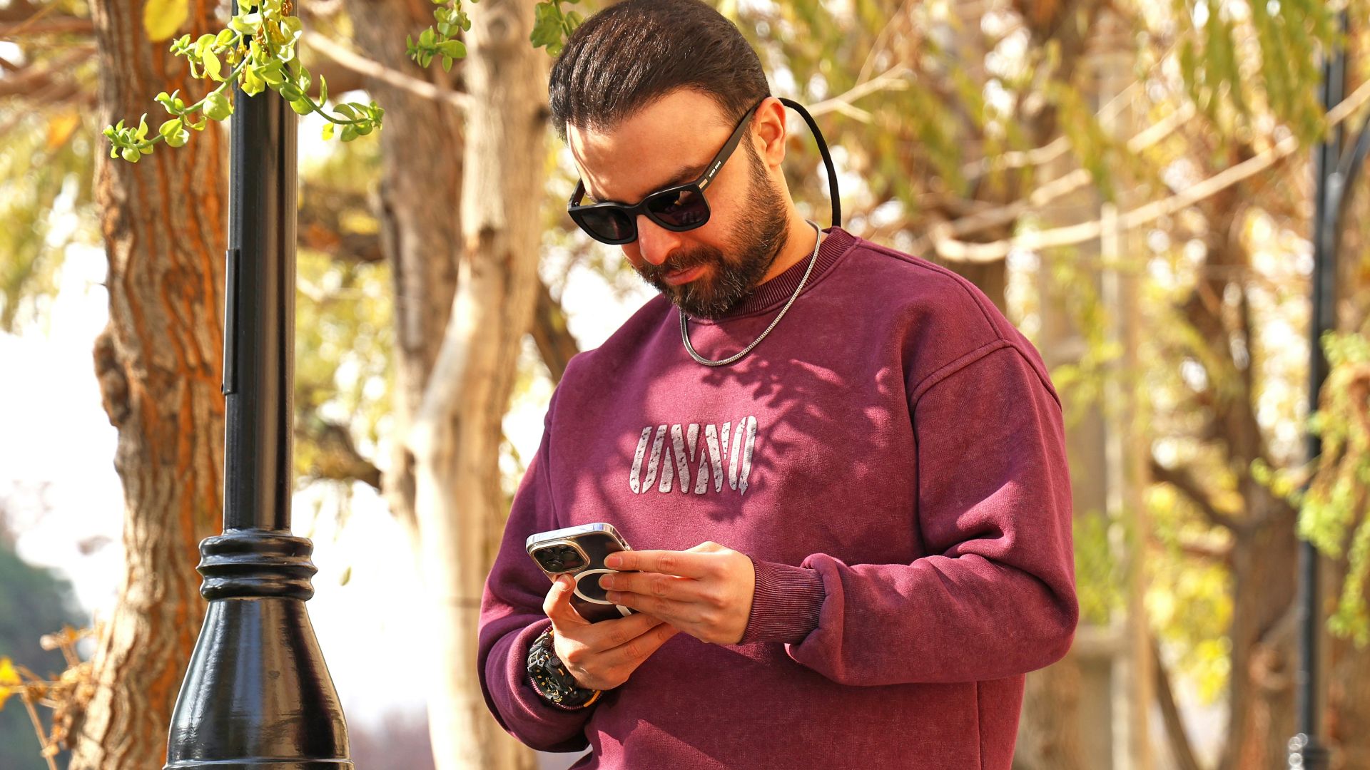 Man in sunglasses looking at his phone outdoors.