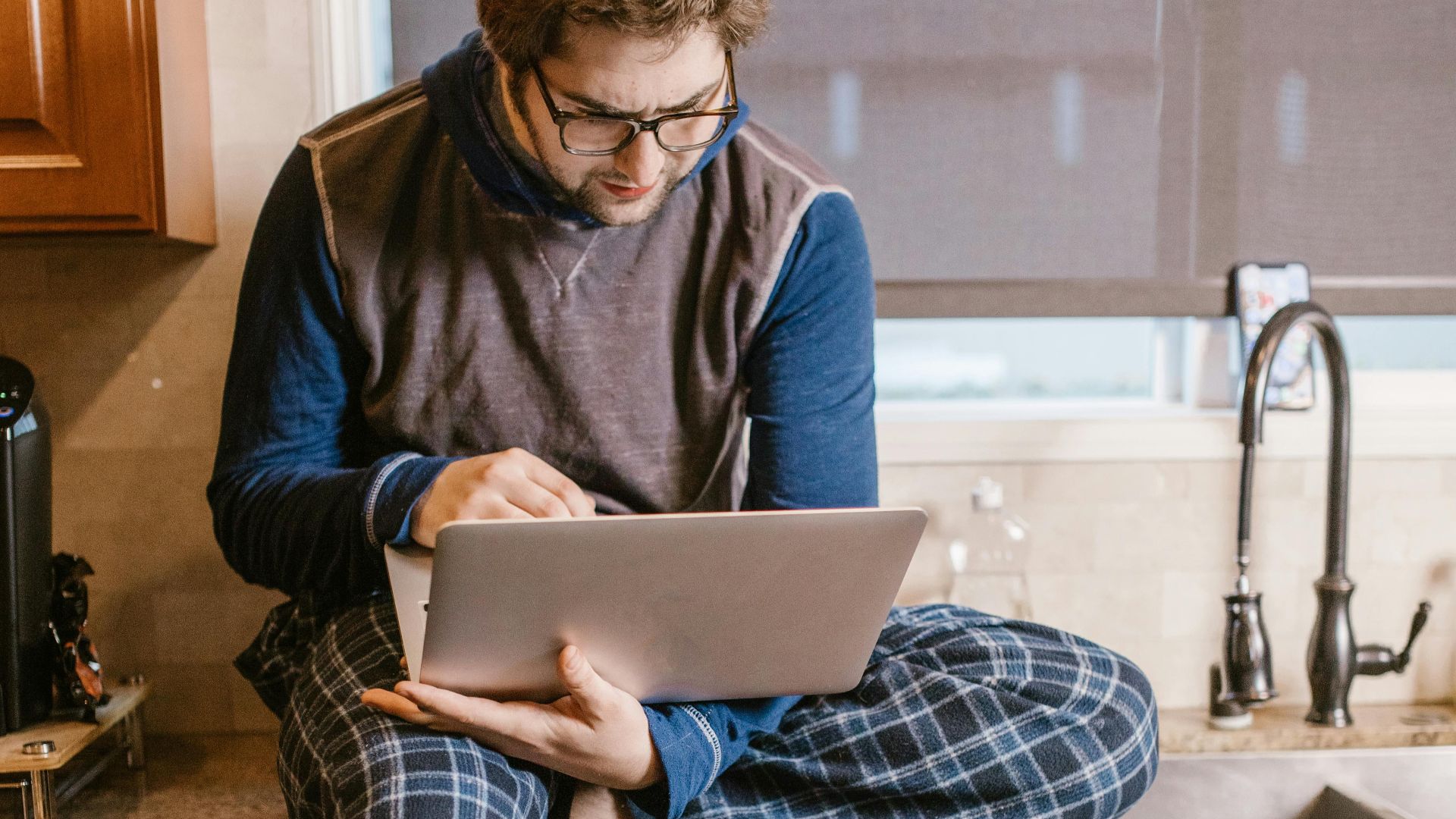Casual man in pajamas working on a laptop while sitting on the kitchen counter.
