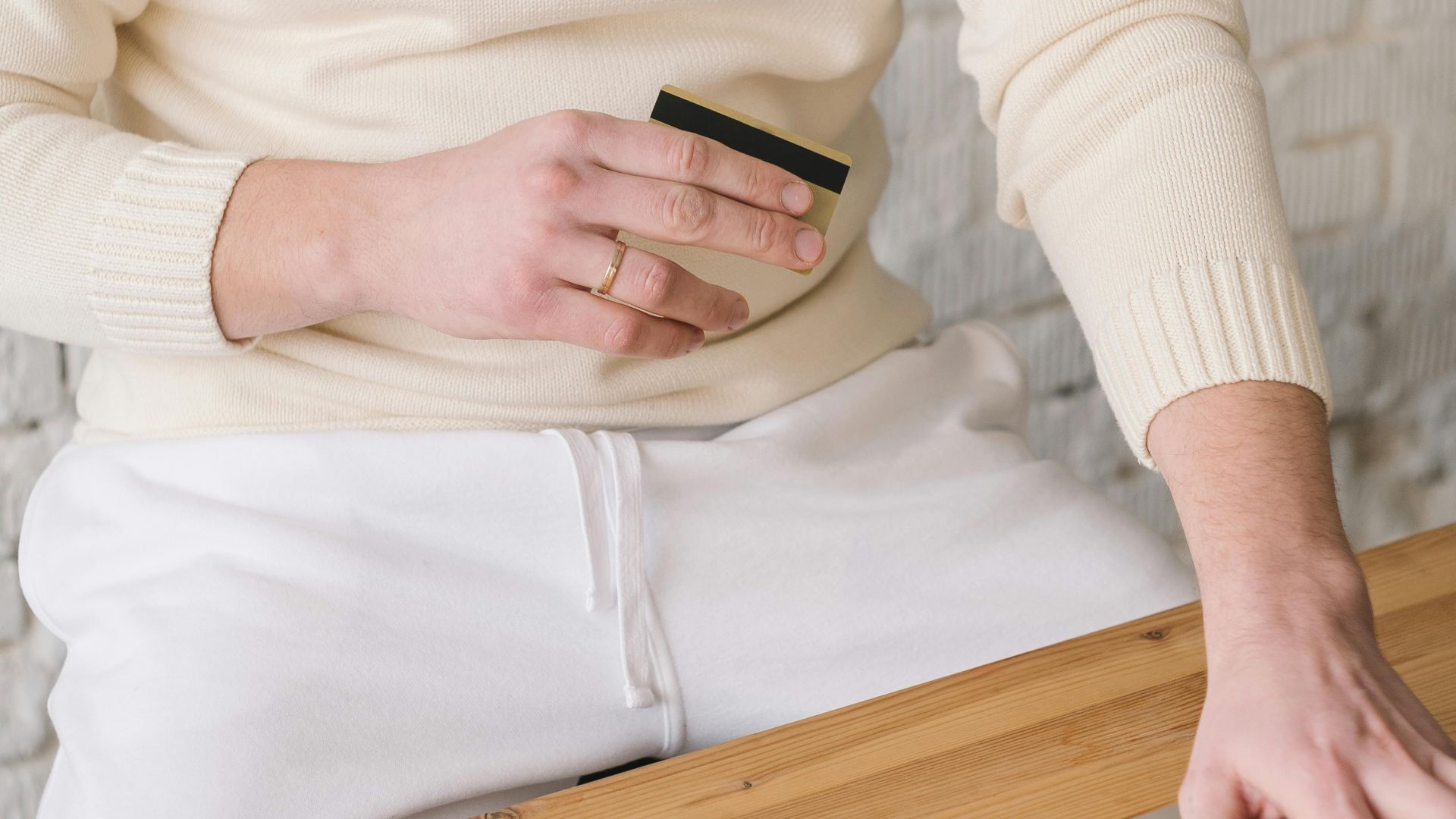 Adult man using laptop and holding credit card for online shopping in a minimalistic setting.