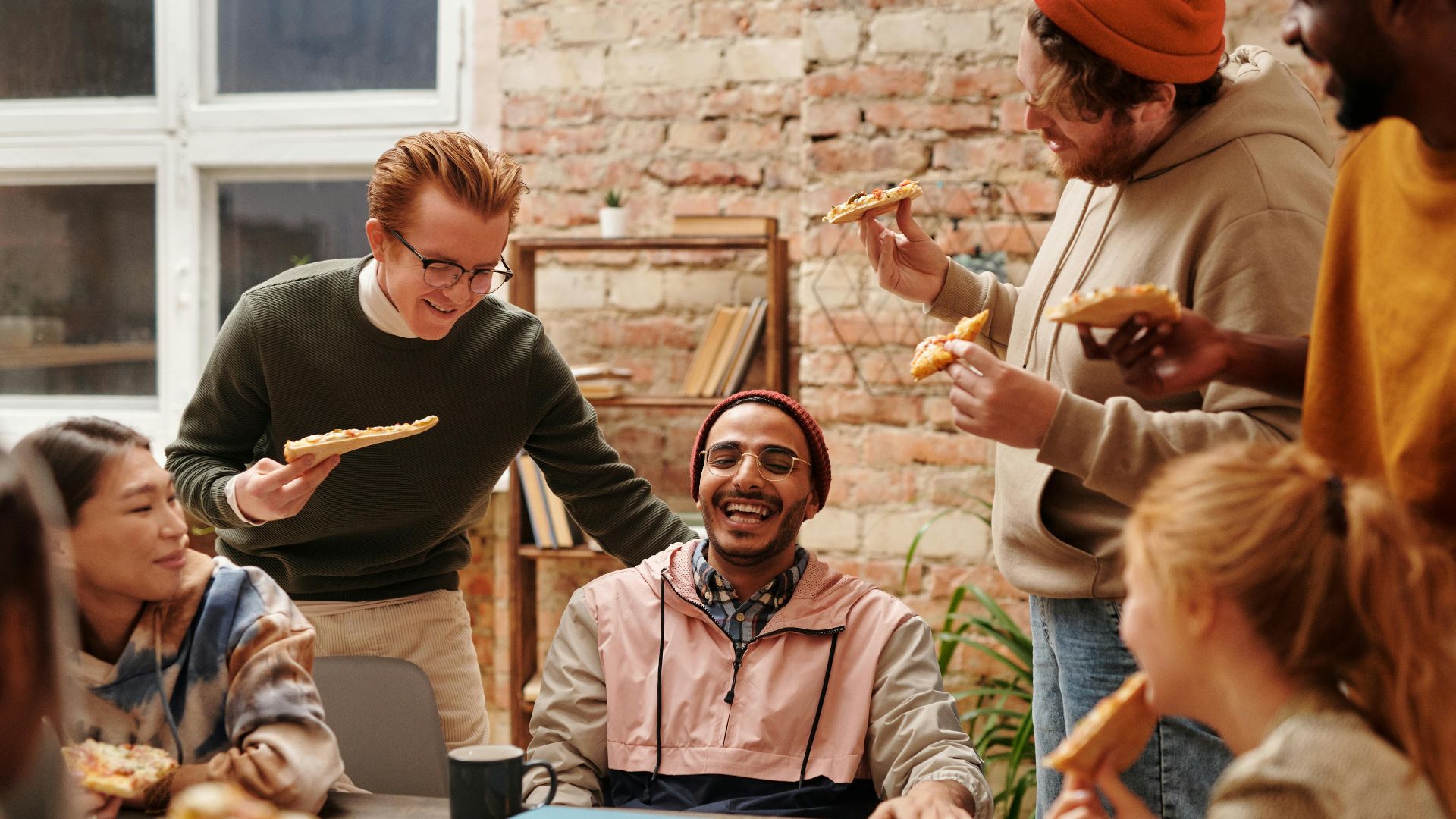 A joyful group of diverse friends enjoying pizza together in a cozy indoor setting.
