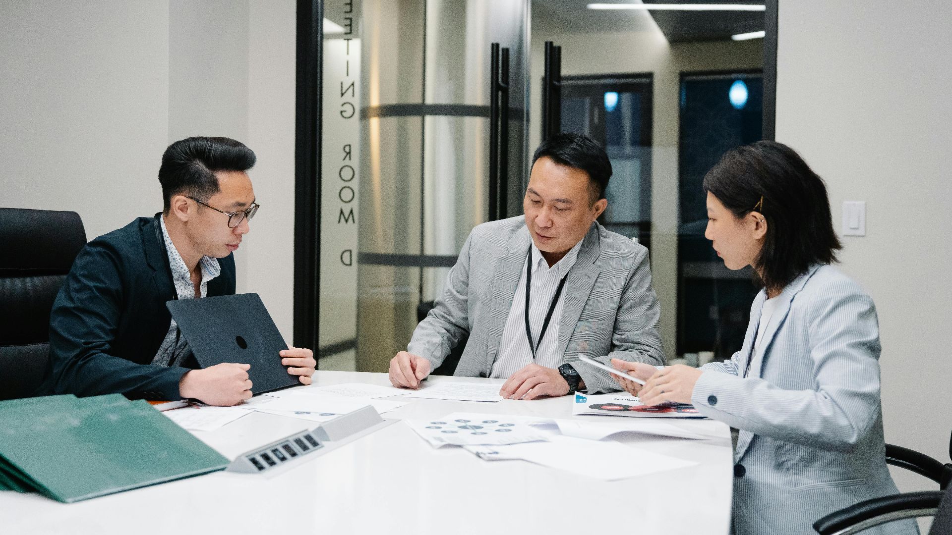 Business meeting with three professionals collaborating in a modern conference room setting.