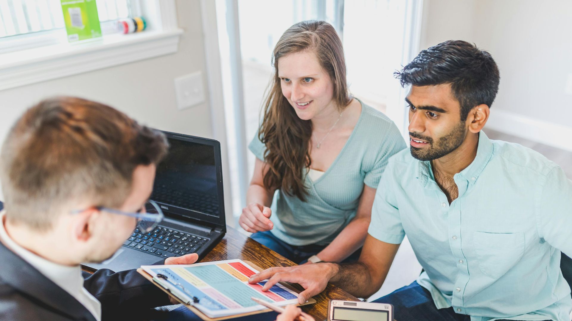 A couple consults with a real estate agent about buying a new home, papers and calculator on the table.