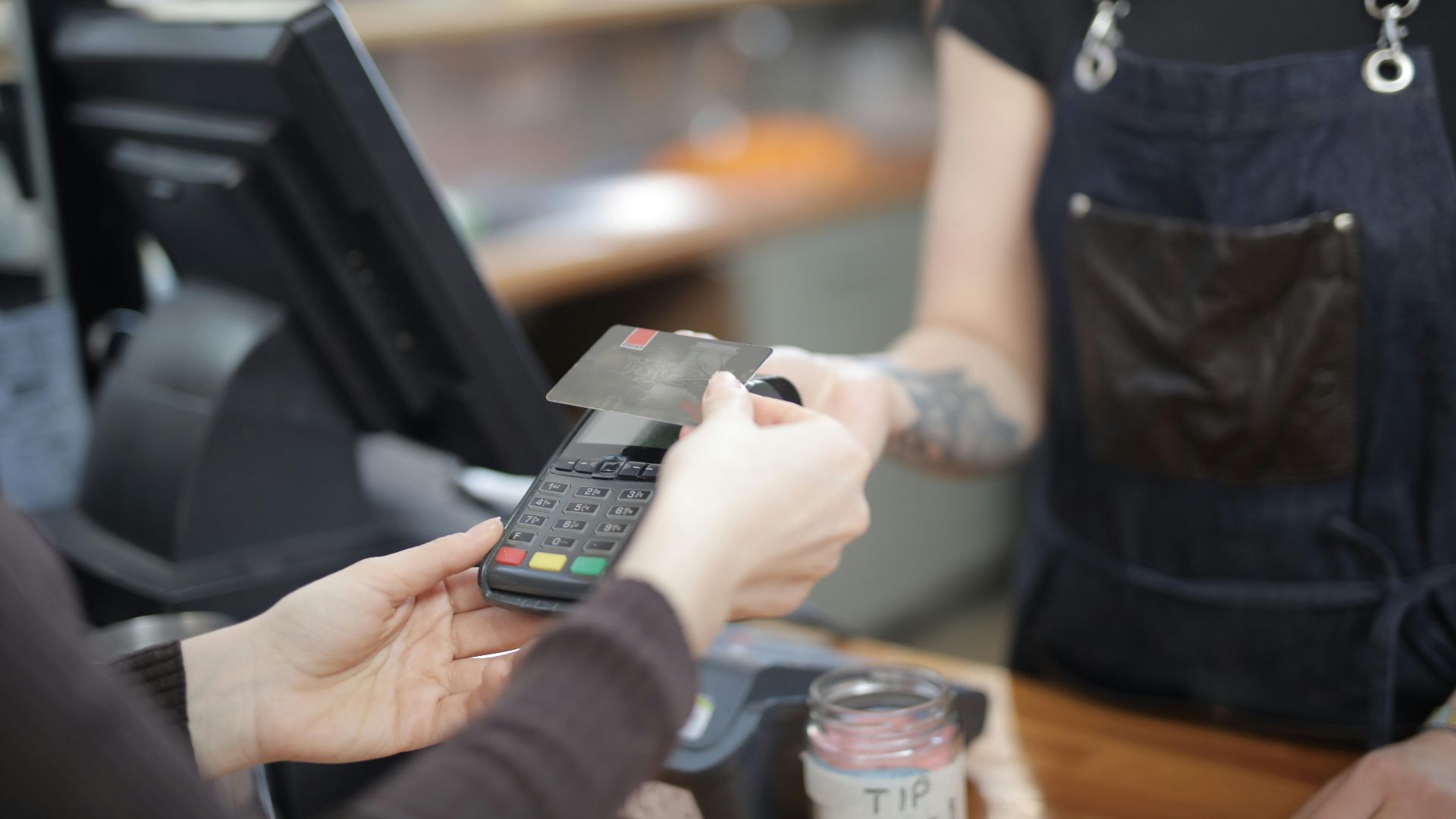 Close-up of customer and cashier during a credit card transaction at a store counter indoors.