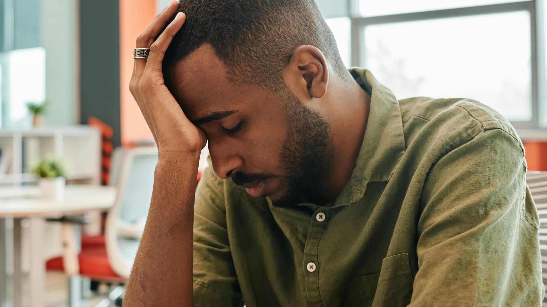 African American man experiencing burnout at office desk with a laptop.