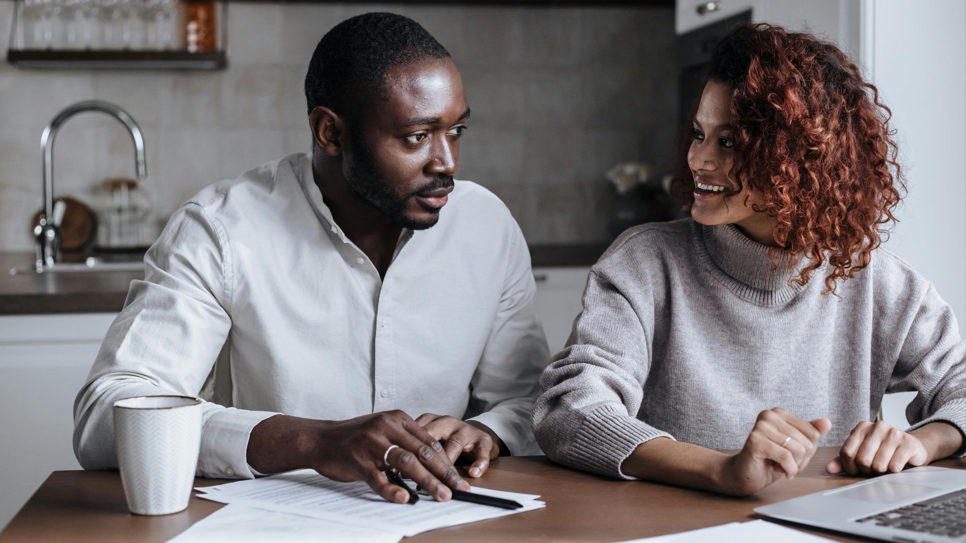 Black couple collaborating on a project at their kitchen table, showcasing teamwork and home office lifestyle.