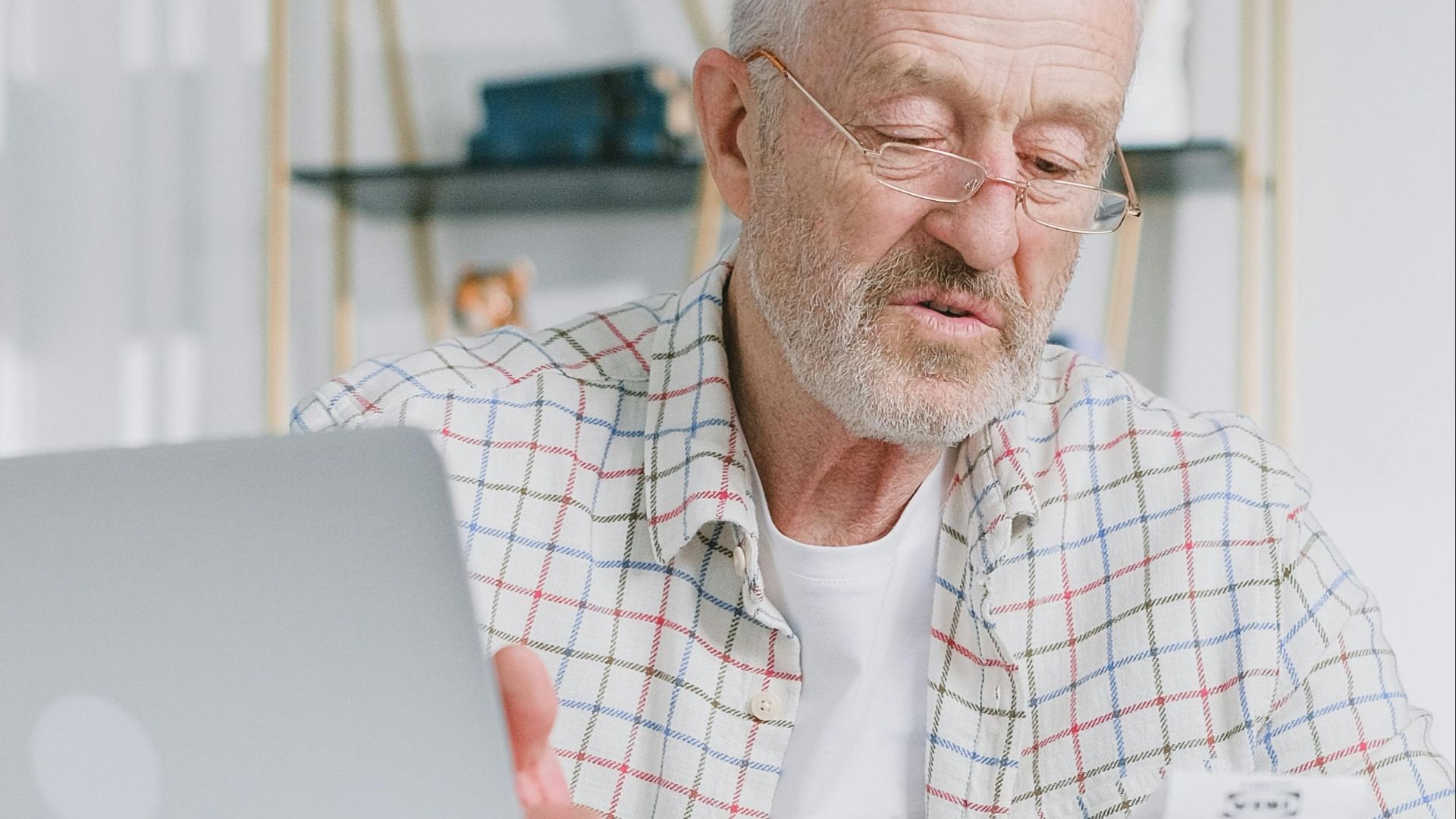Elderly man reading papers at home with a laptop, emphasizing financial planning.
