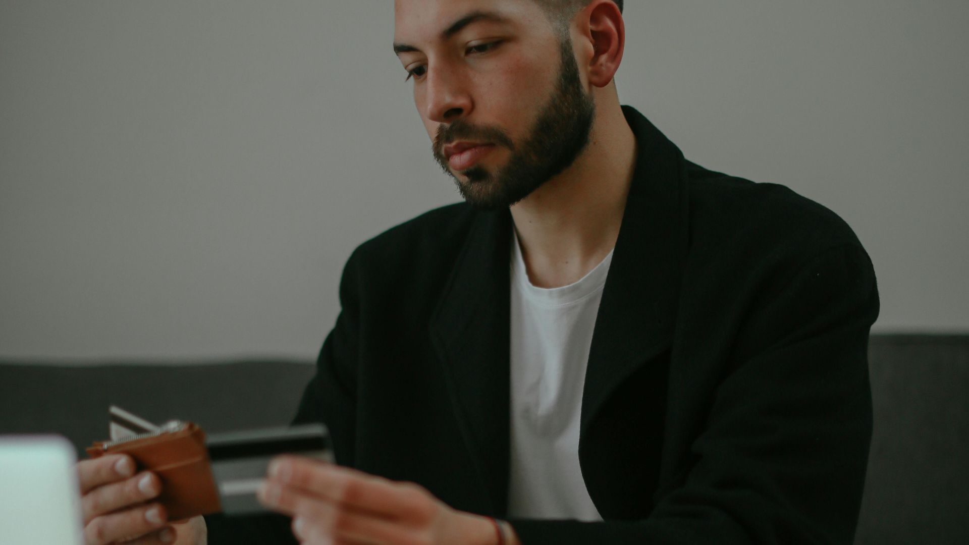 A young man with a beard uses a credit card for online shopping at home.