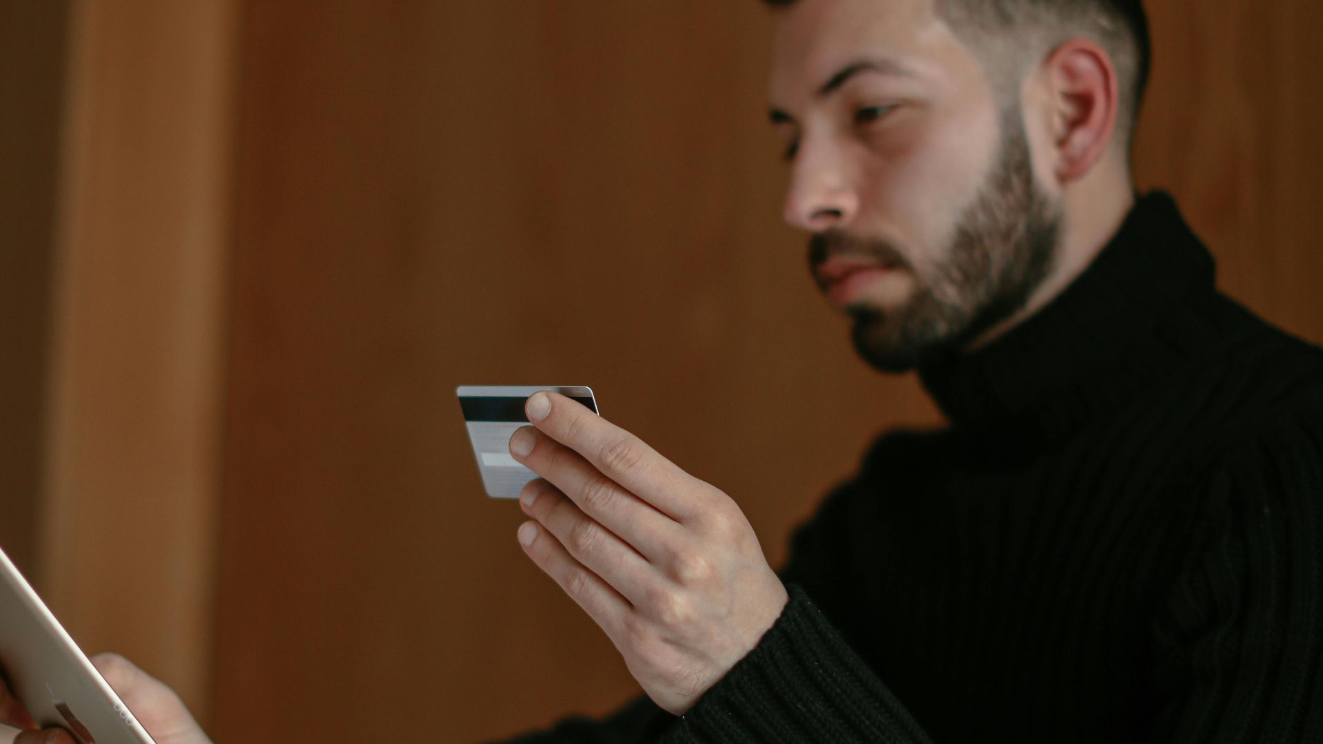Bearded adult man using a tablet and credit card for online shopping at home.