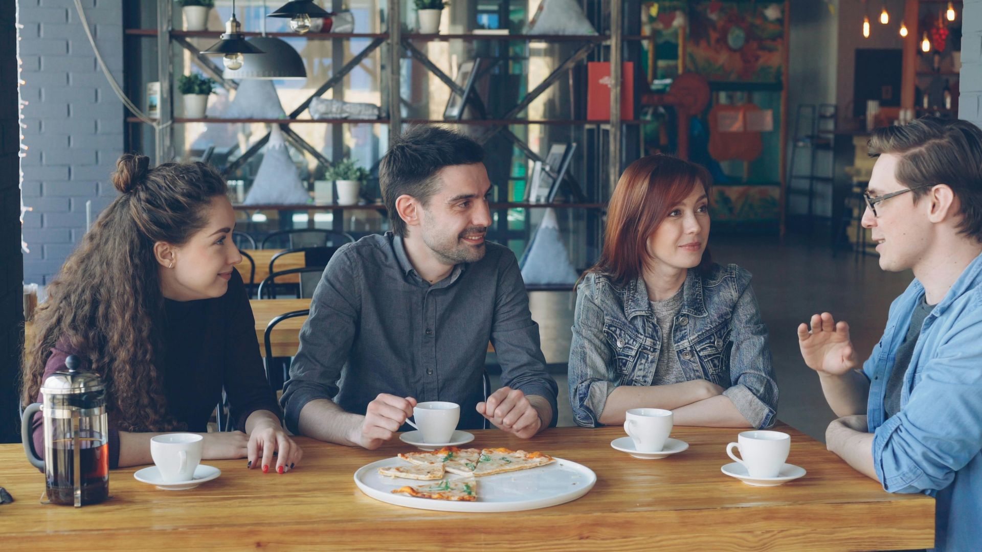 Group of young adults enjoying coffee and pizza in a trendy cafe.