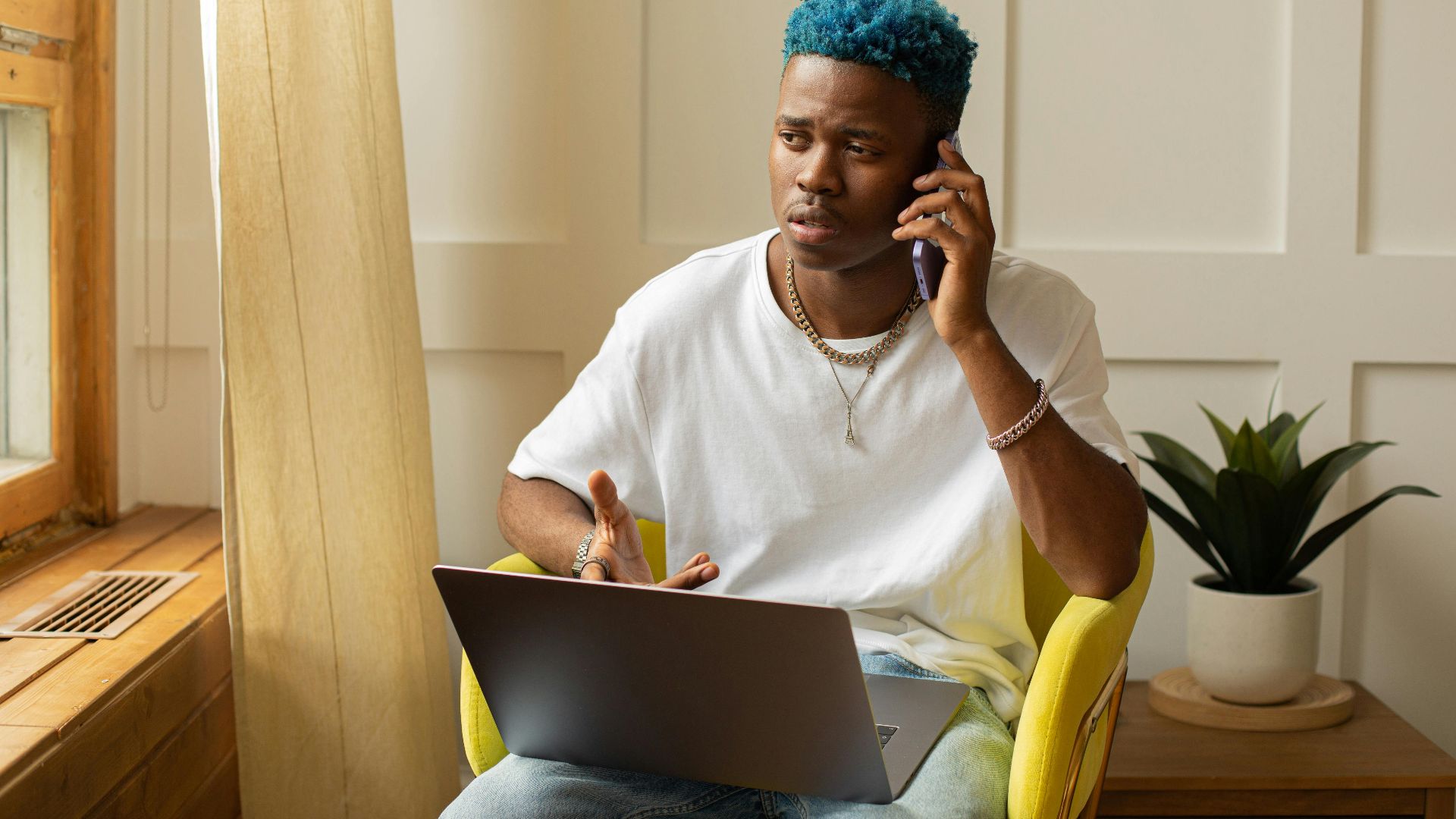African American man working remotely on laptop while on phone call in a sunlit room.