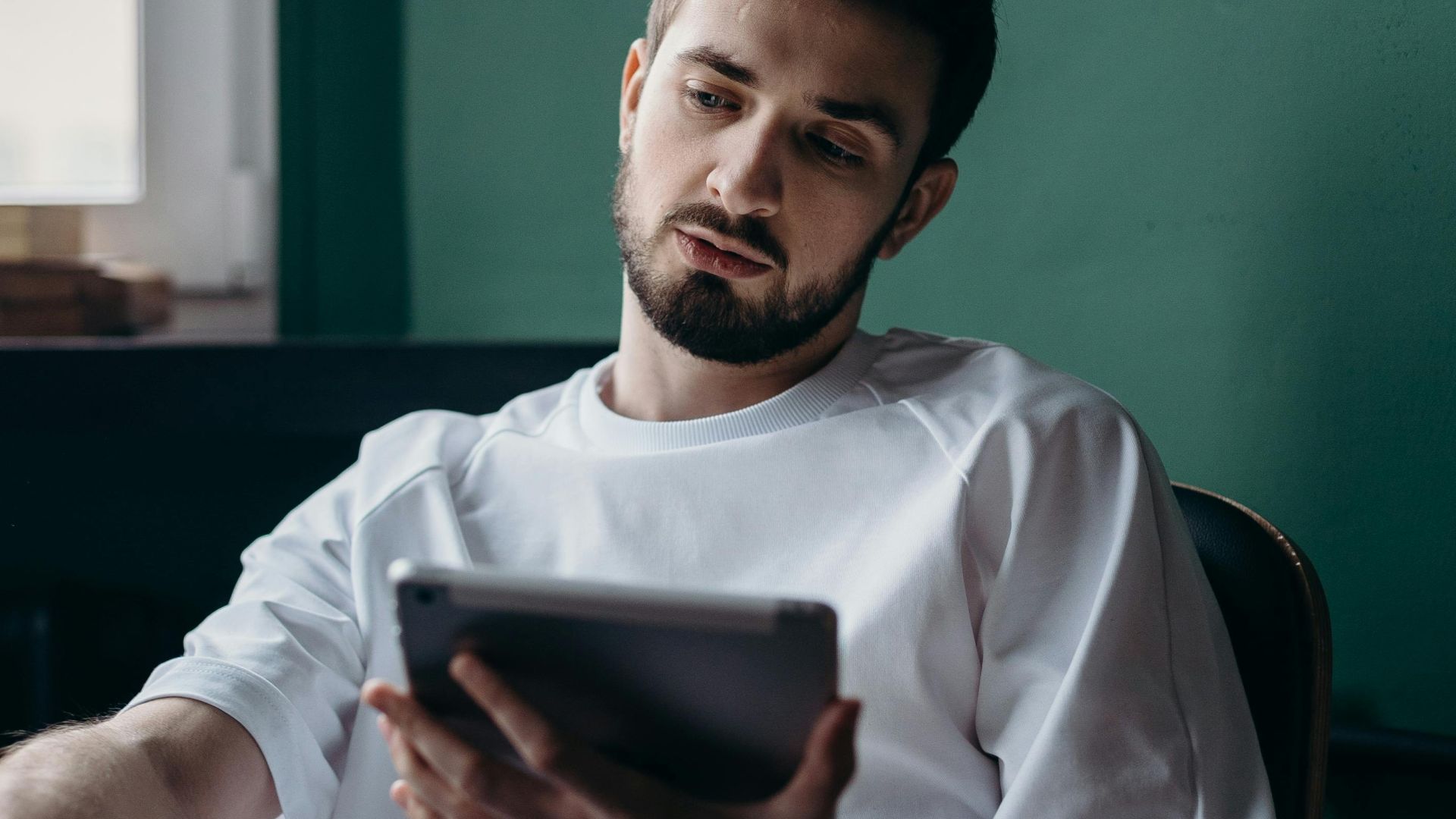 Pensive man using a tablet while relaxing at home. Modern lifestyle concept.