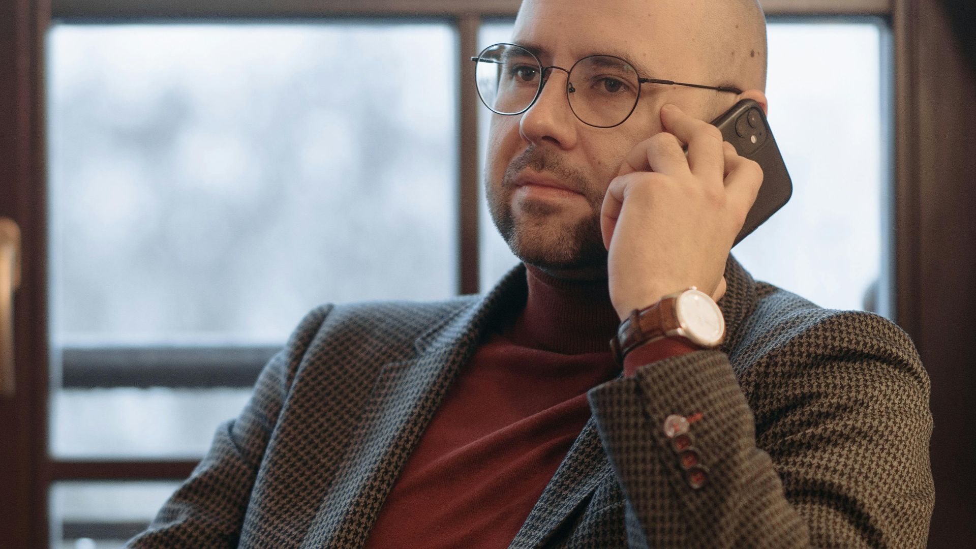 Bald man in formal attire using a smartphone in a stylish office.