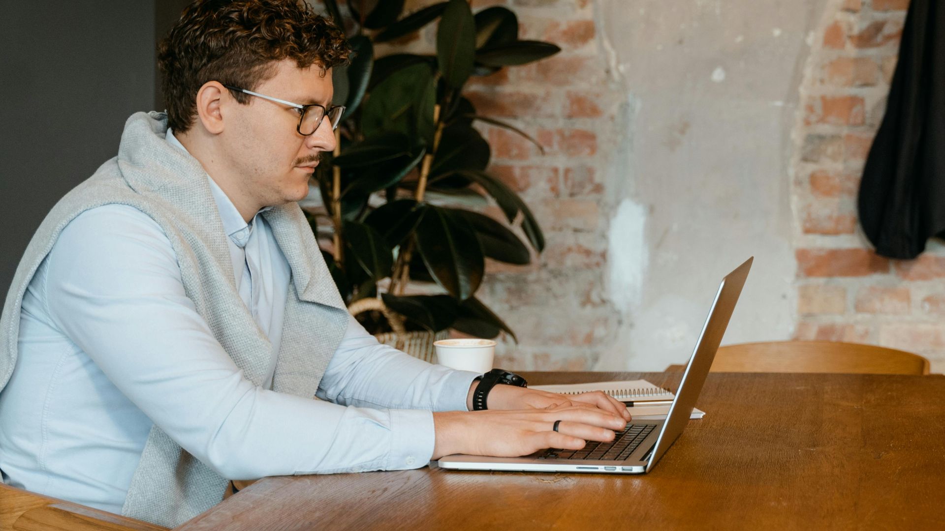 Focused caucasian man with eyeglasses using laptop at wooden table in modern office