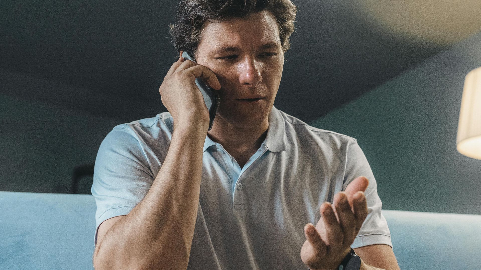 Man speaking on a smartphone while sitting on a sofa, working from home.