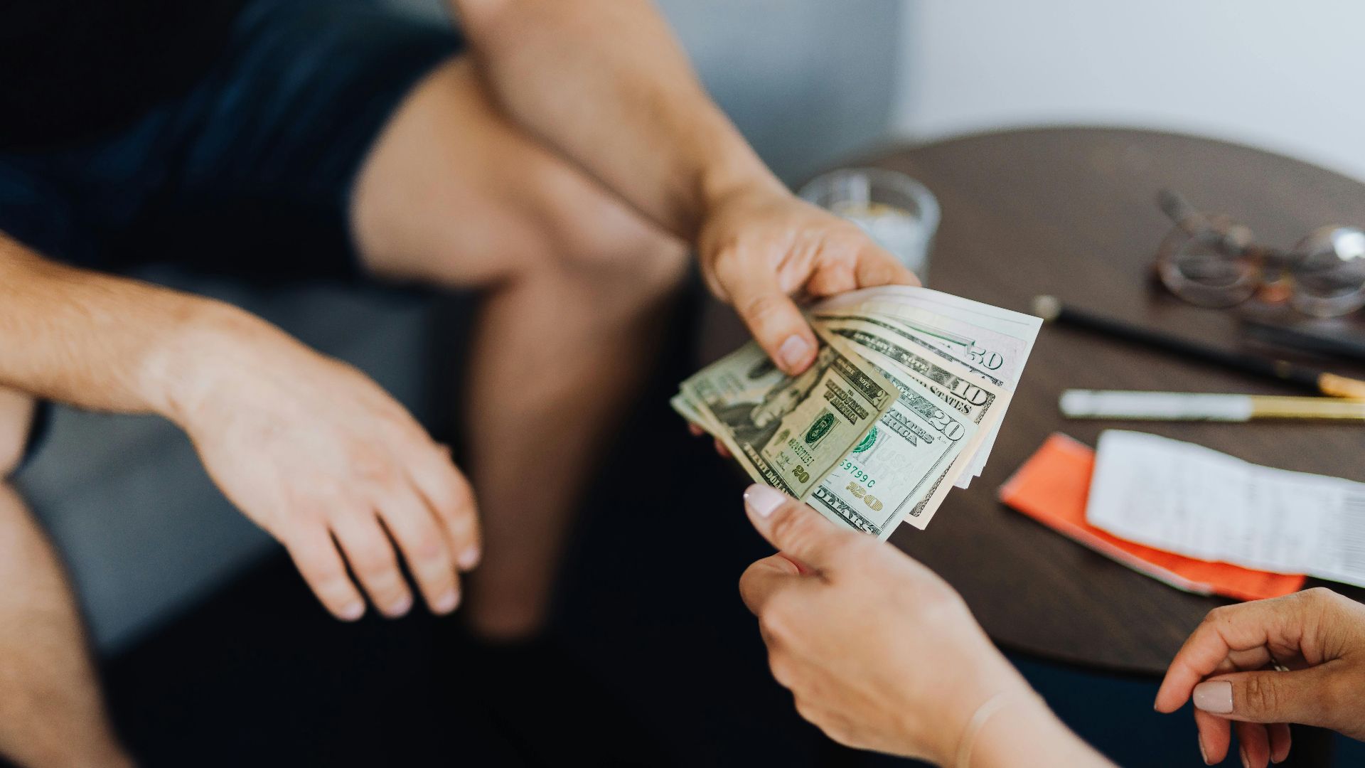 Close-up of hands exchanging US dollar bills, symbolizing a financial transaction or payment.