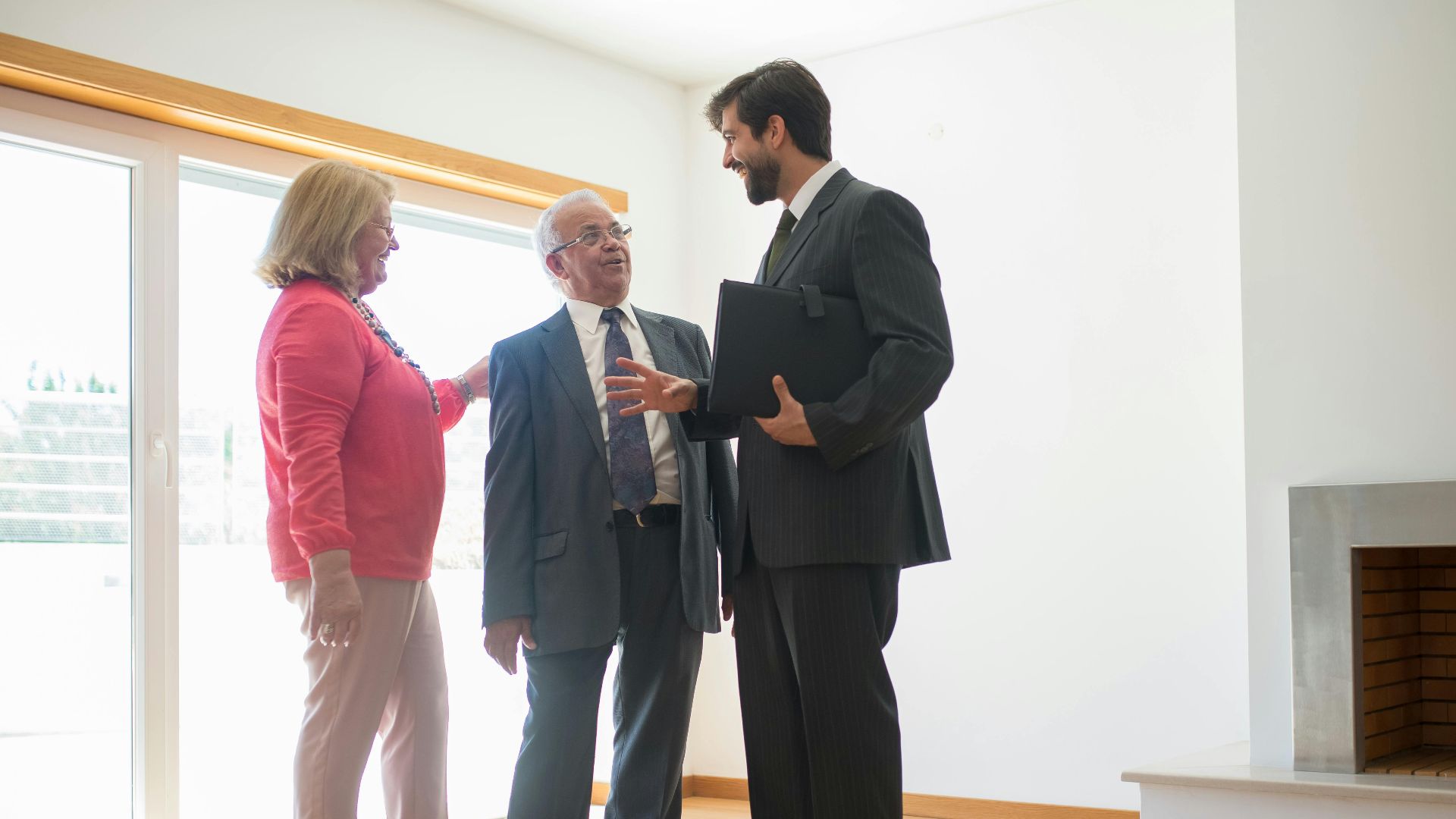 A real estate agent shows an empty house to senior clients, highlighting the spacious room.