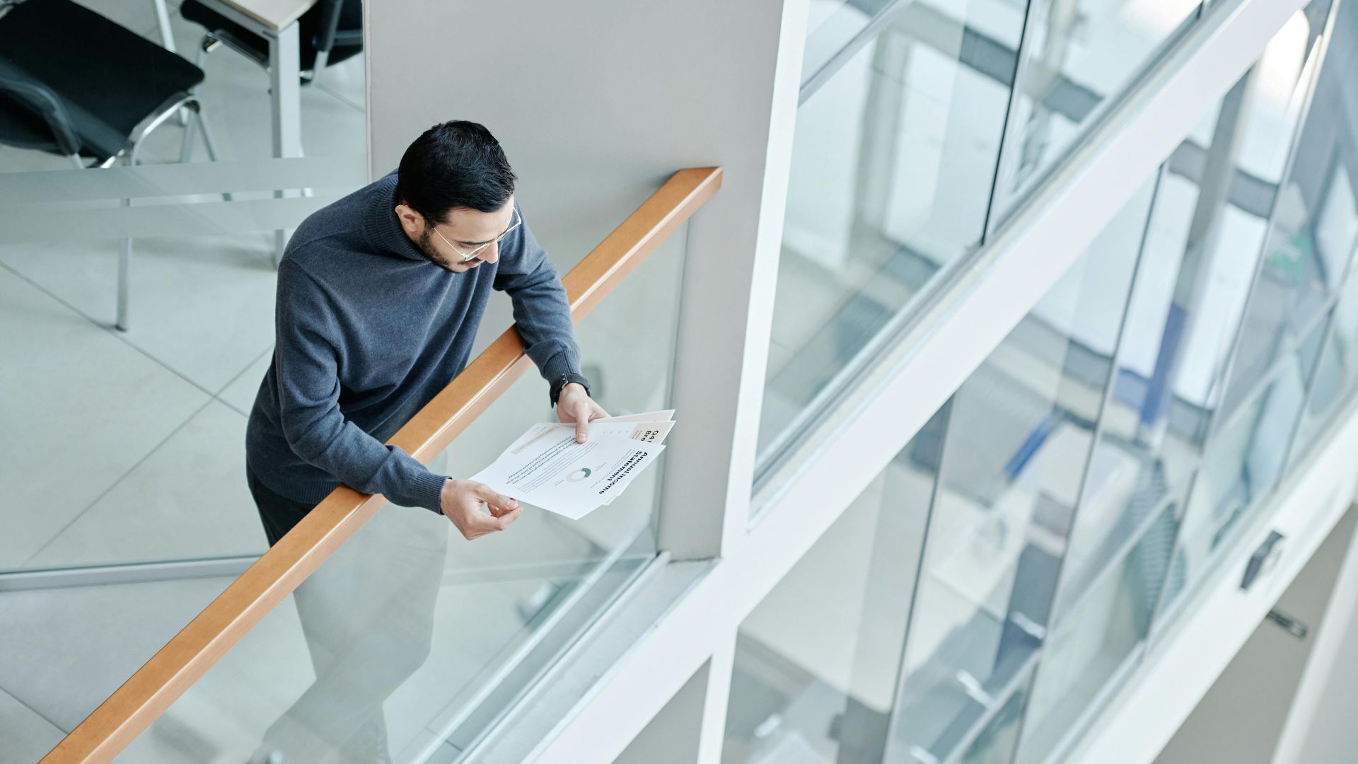 A professional man examines papers in a bright, contemporary office space with glass walls.