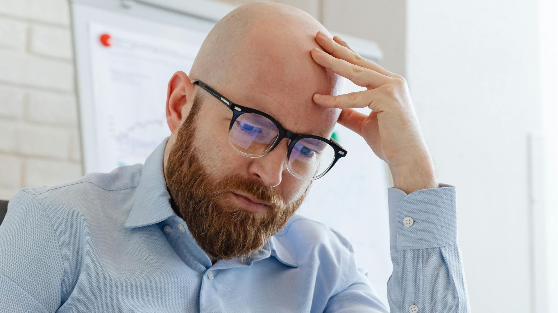 Caucasian businessman with beard and glasses reviewing documents in a modern office setting.