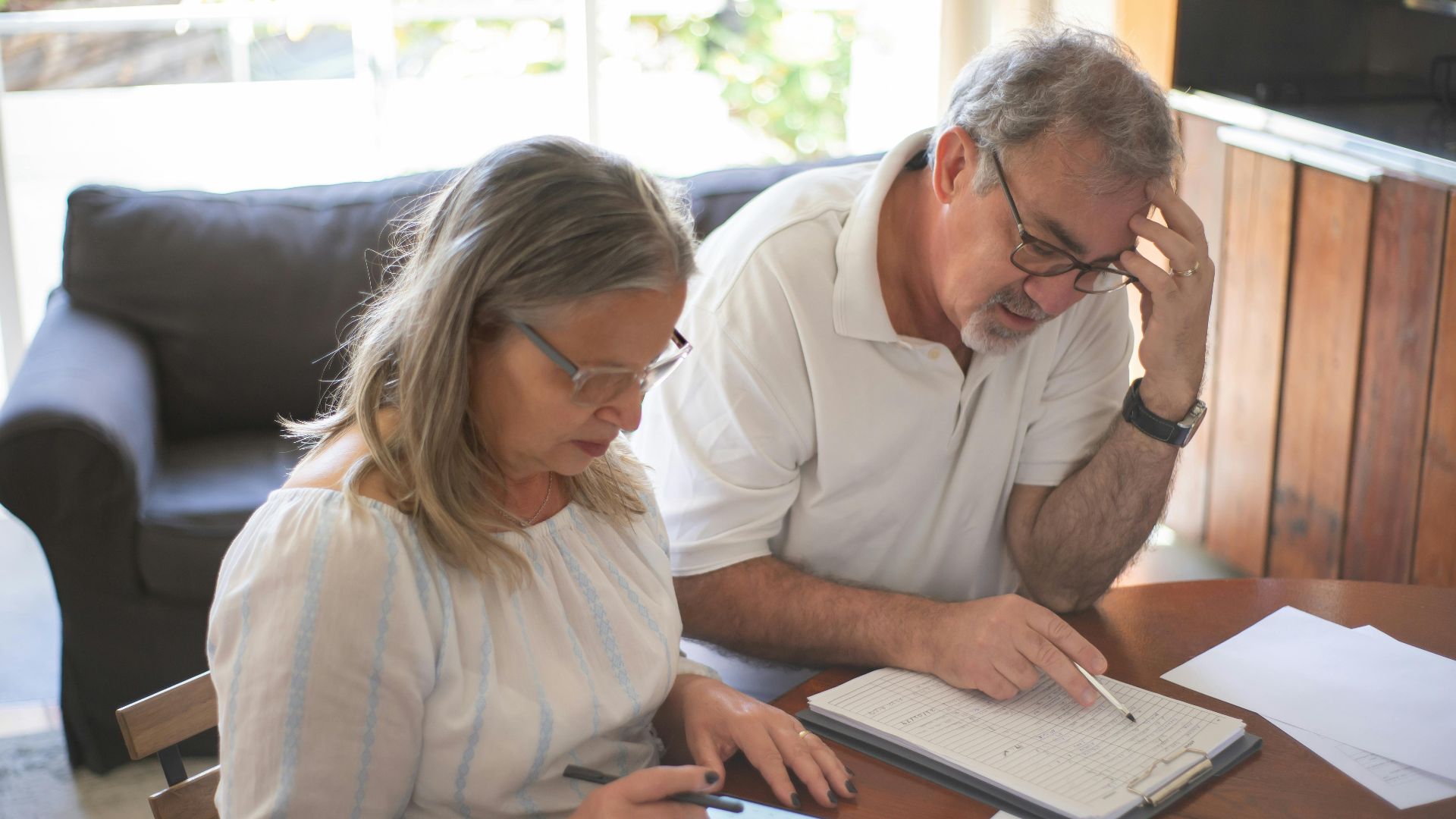 Elderly couple reviewing bills and documents at home, focusing on finances and technology.