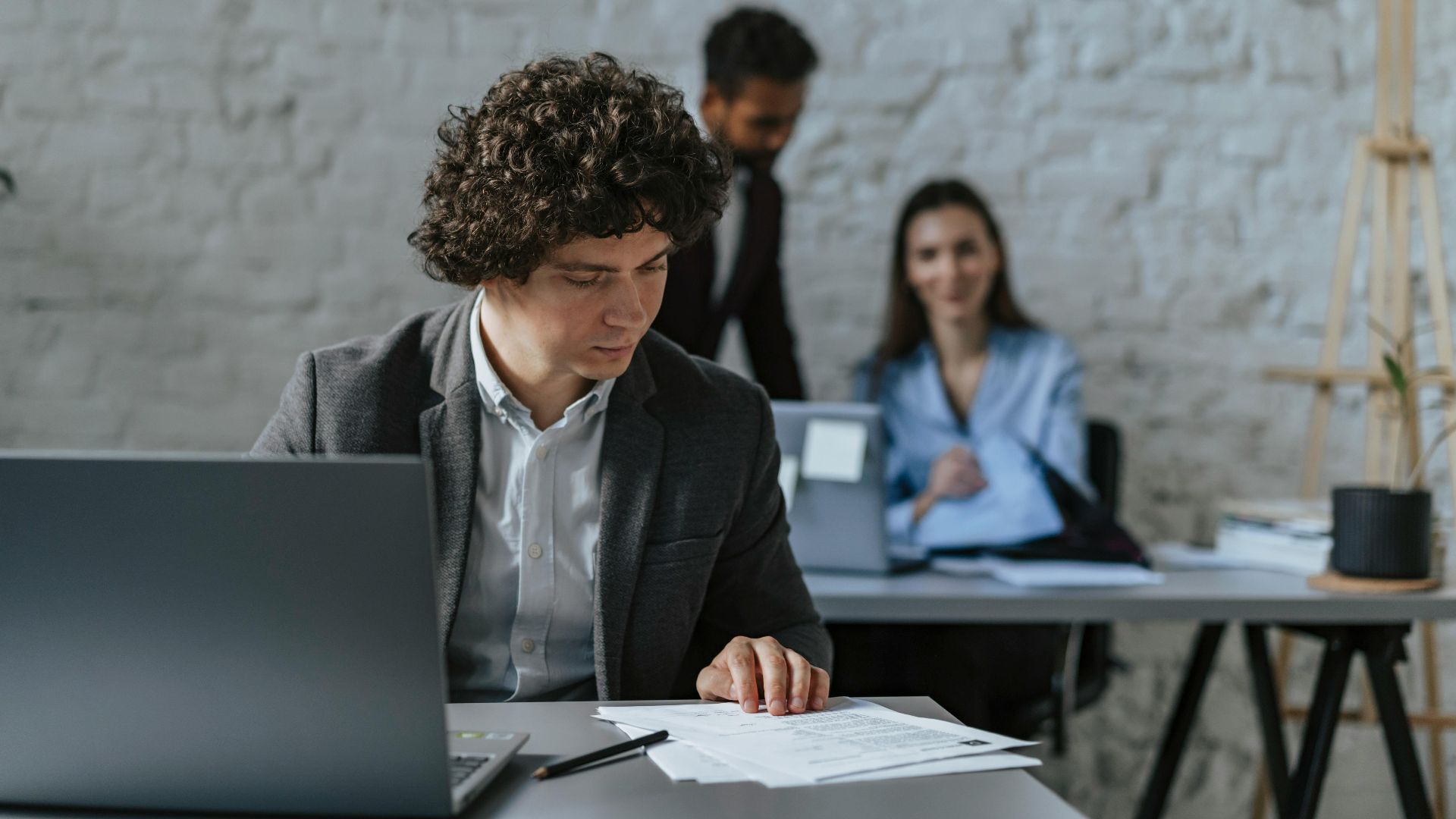 Business professionals working together in a modern office setting with focus on curly-haired man reviewing documents.
