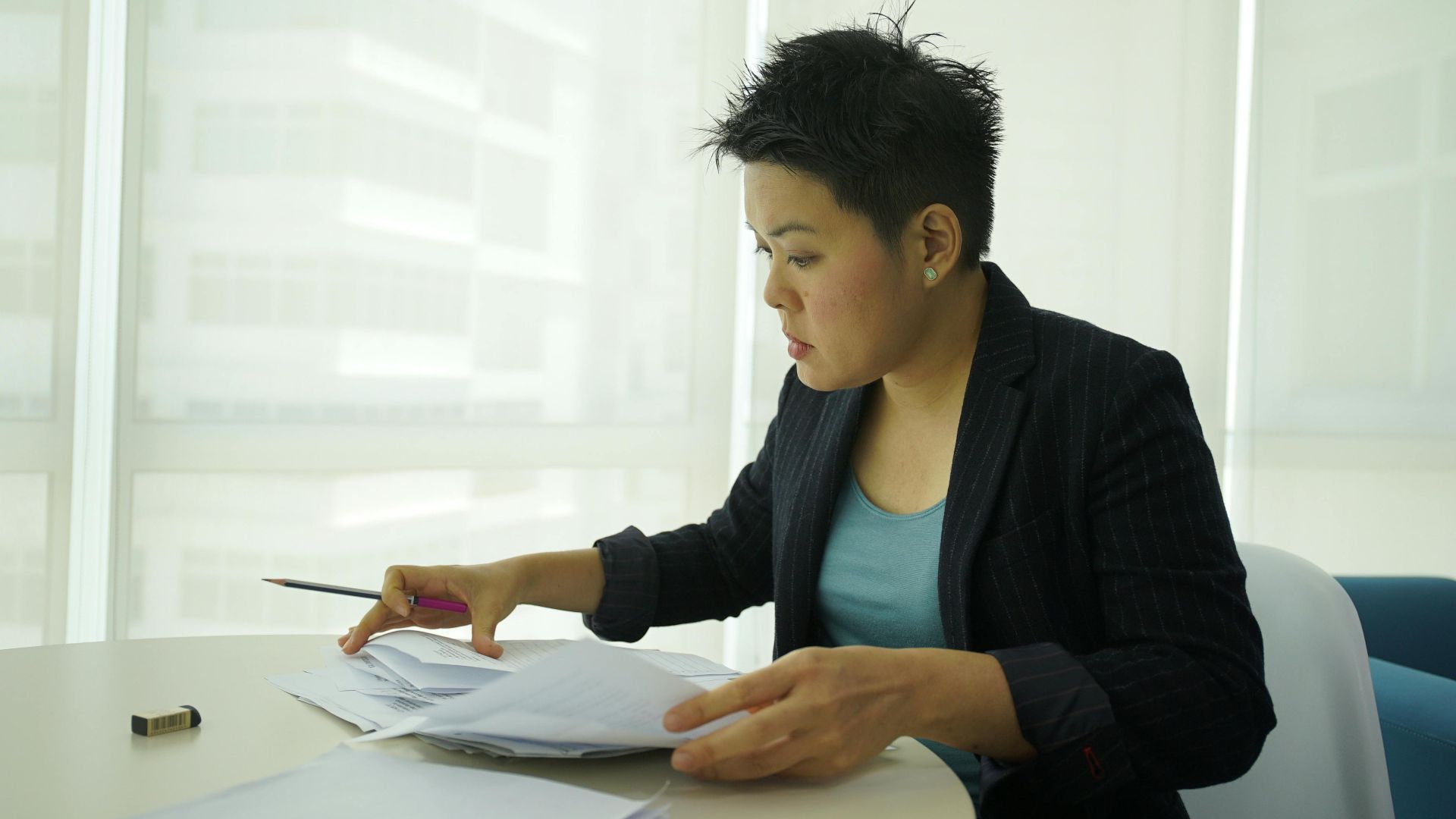 Businesswoman reviewing documents at a round table in a bright office space.