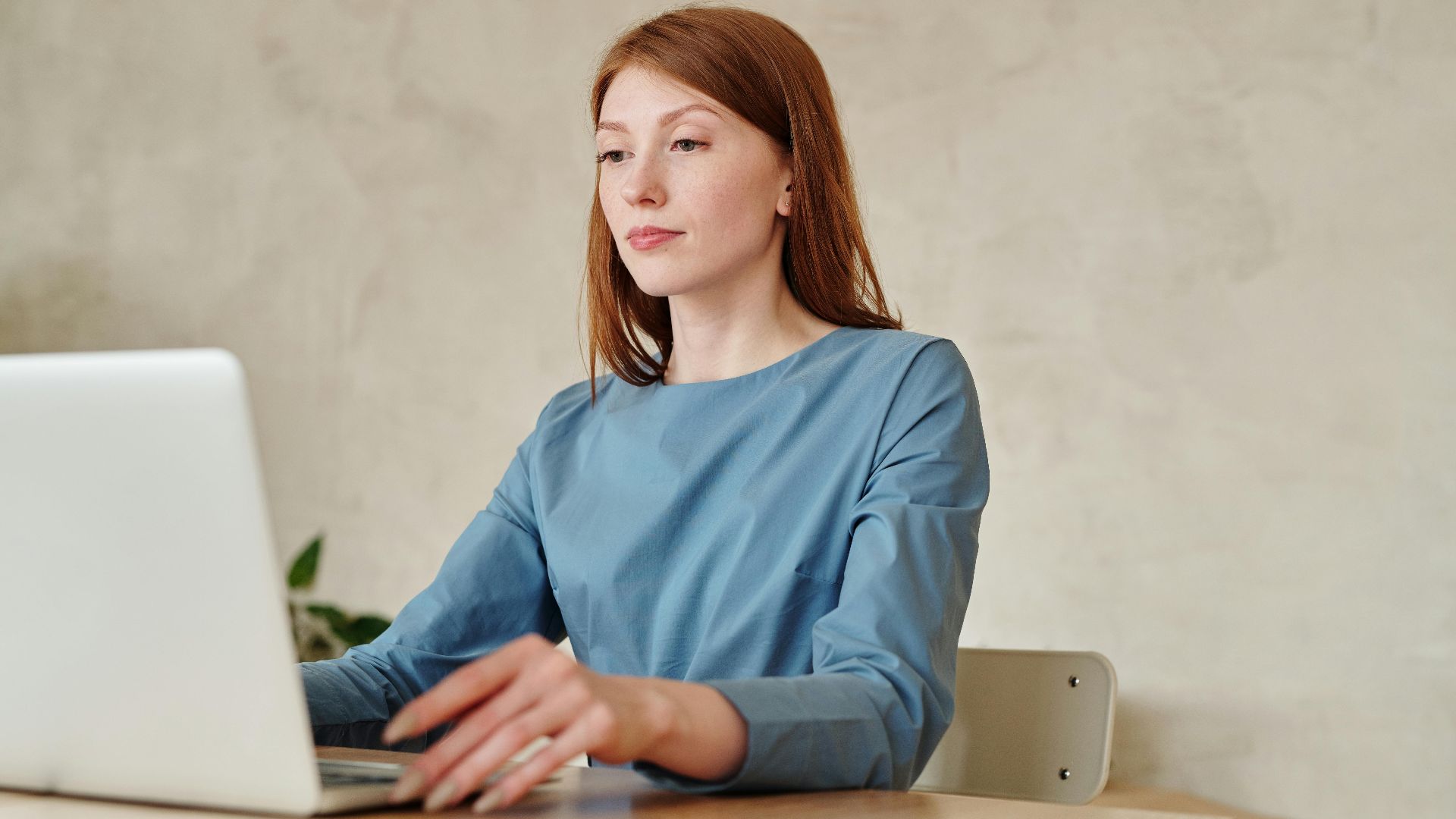Caucasian woman in blue shirt working on a laptop indoors at home.