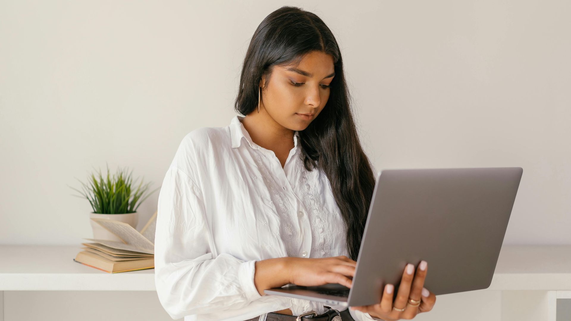 A young woman typing on a laptop while standing indoors, focused and professional.