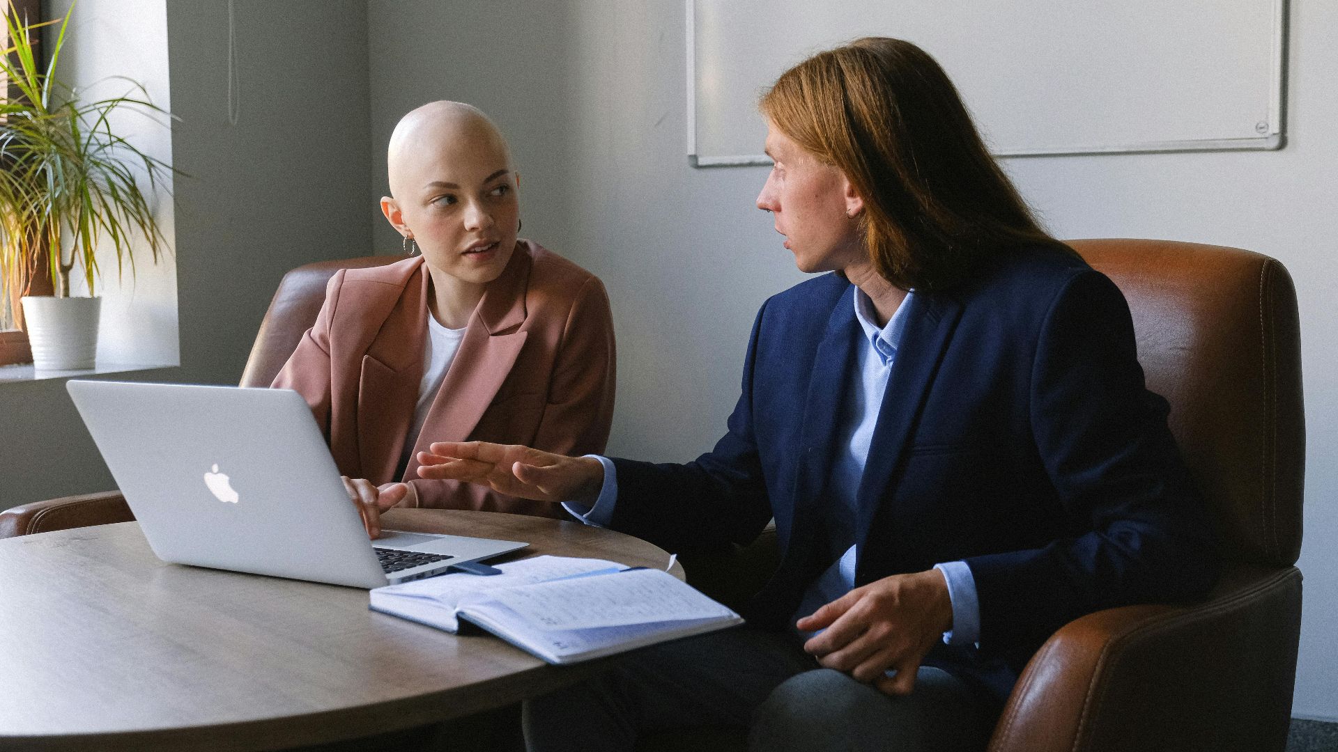 Confident young coworkers wearing formal jackets sitting in leather armchairs near table with netbook and organizer while sharing business ideas