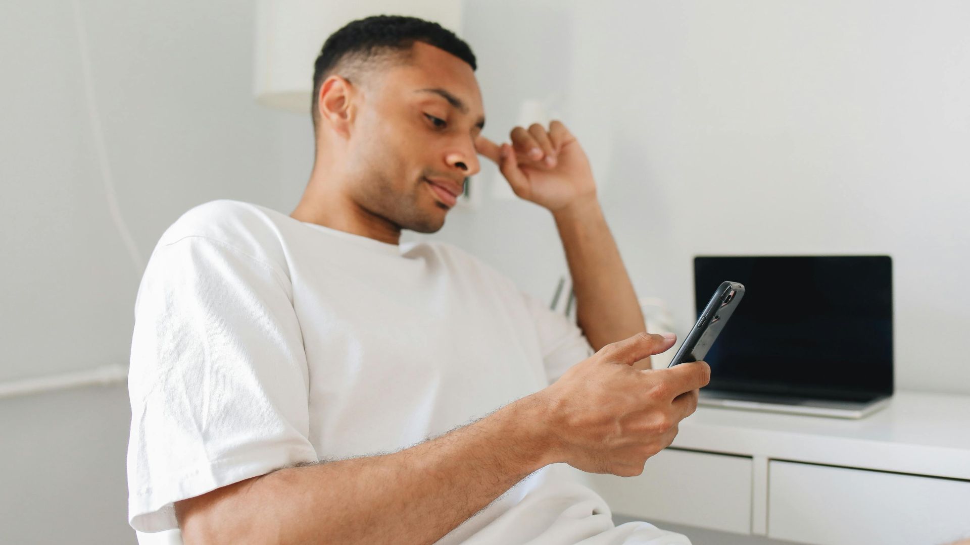 Casual man in white shirt browsing on smartphone indoors, showcasing modern lifestyle.