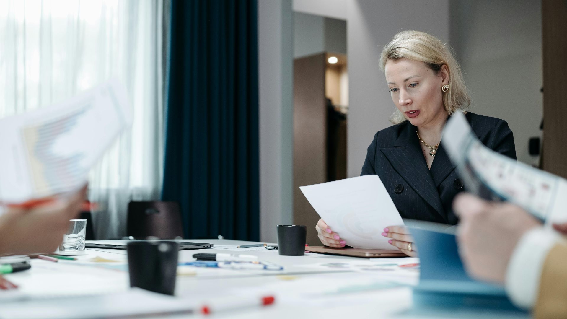 A focused businesswoman reviews paperwork during a professional meeting inside an office.