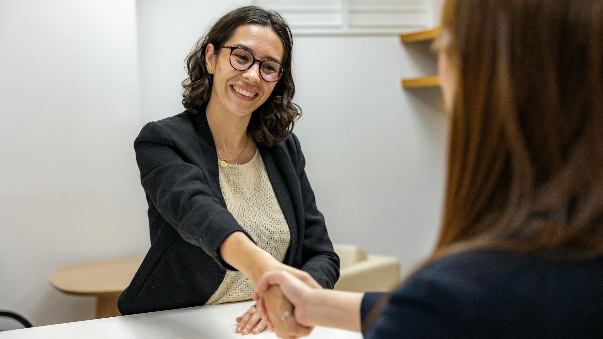 Businesswomen shaking hands in an office, representing a successful job interview or partnership.