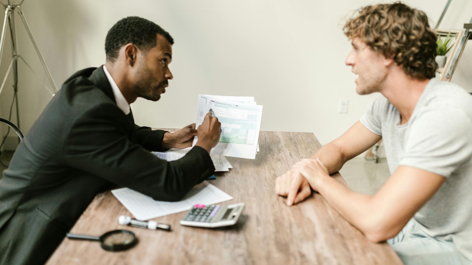 A financial advisor discusses paperwork with a client at a desk in a modern office.