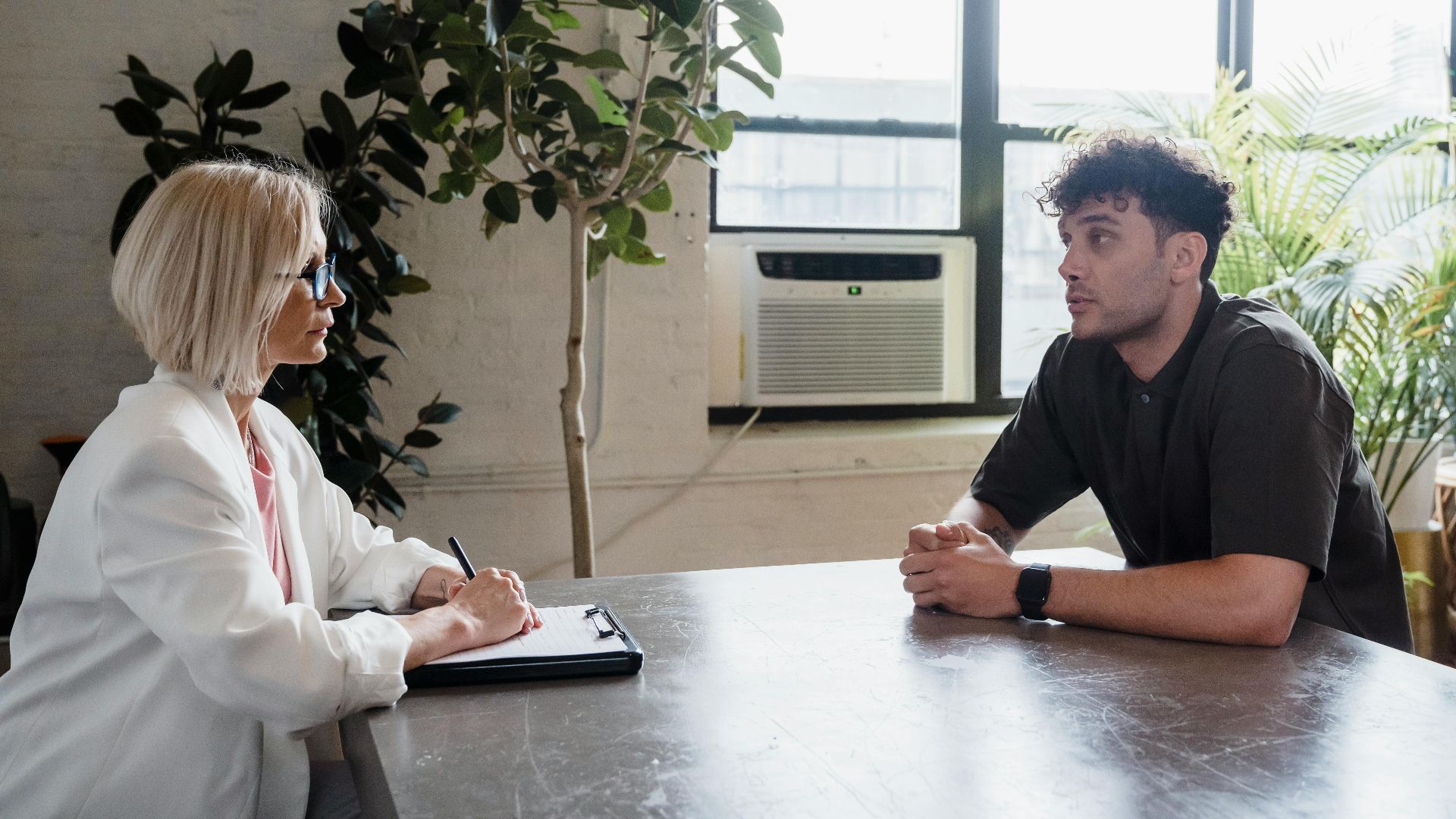 Two professionals engaged in a discussion in a modern office with natural light and plants.