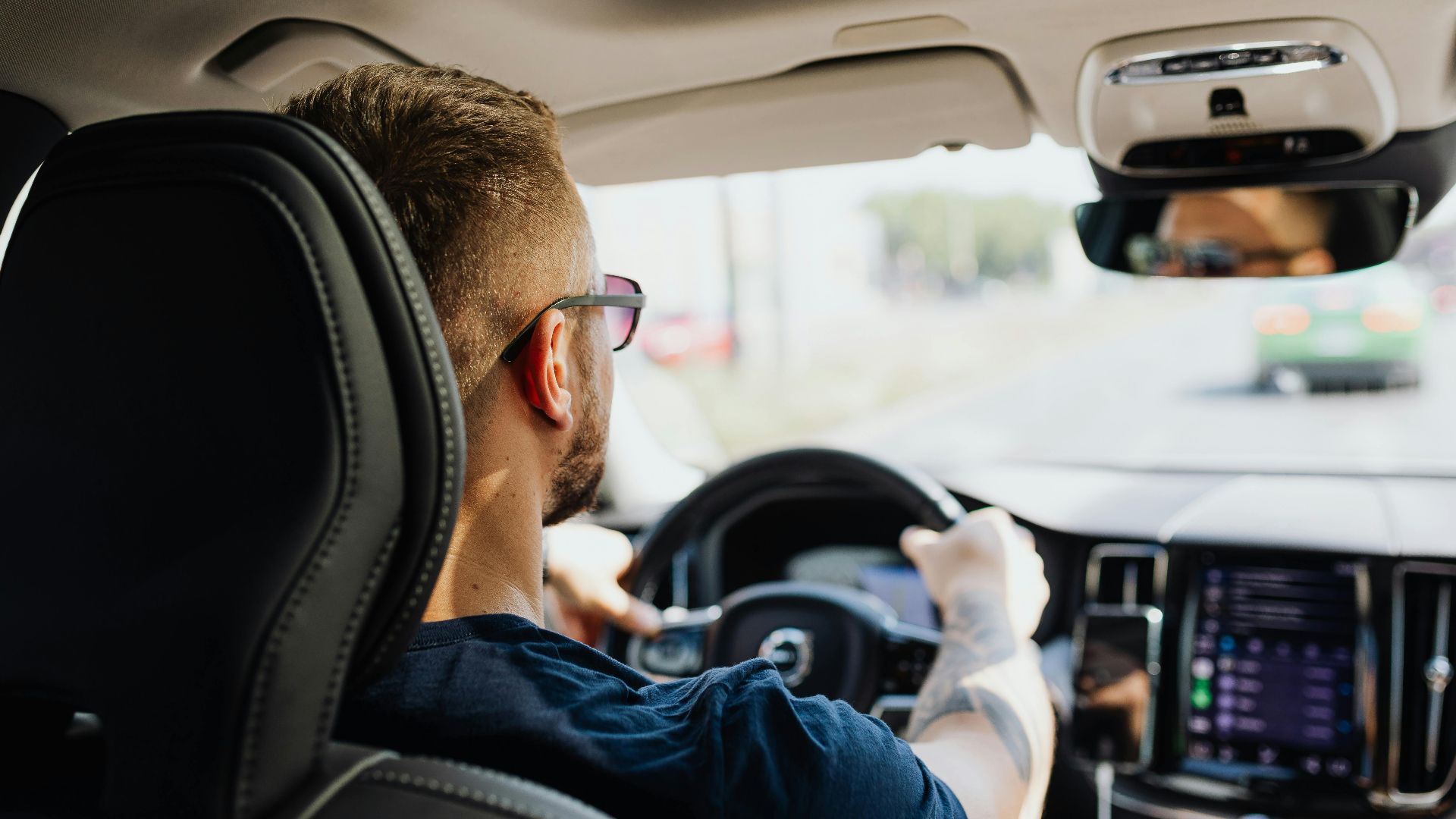 Rear view of a man driving a car with focus on interior details and steering.
