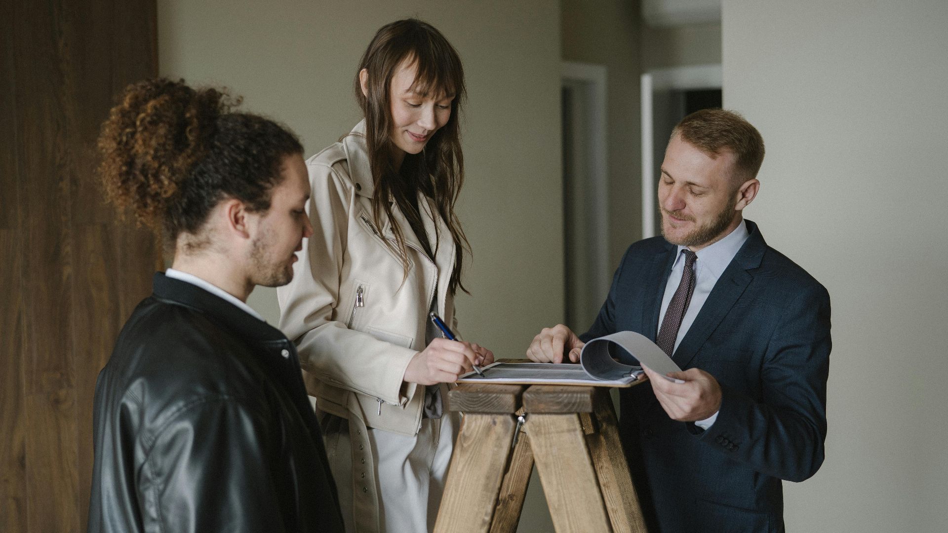 A couple signing real estate documents with a realtor inside a new apartment.