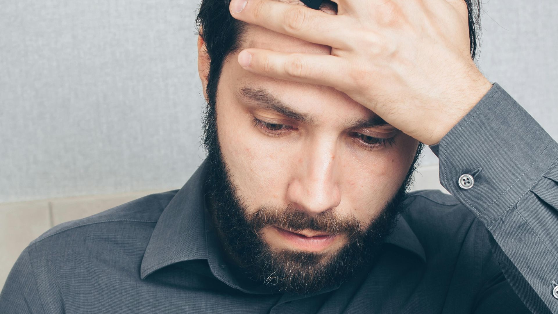 A stressed man looks at his smartphone, holding a credit card in his hand.