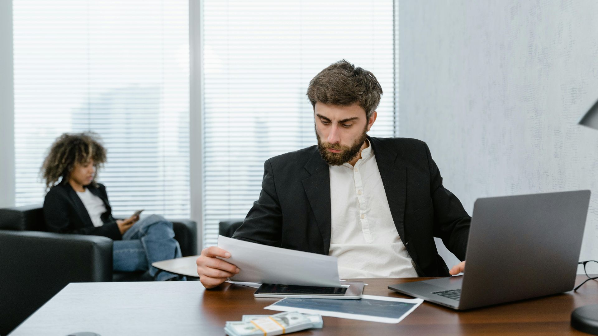 Focused businessman reviews financial reports at office desk with laptop.