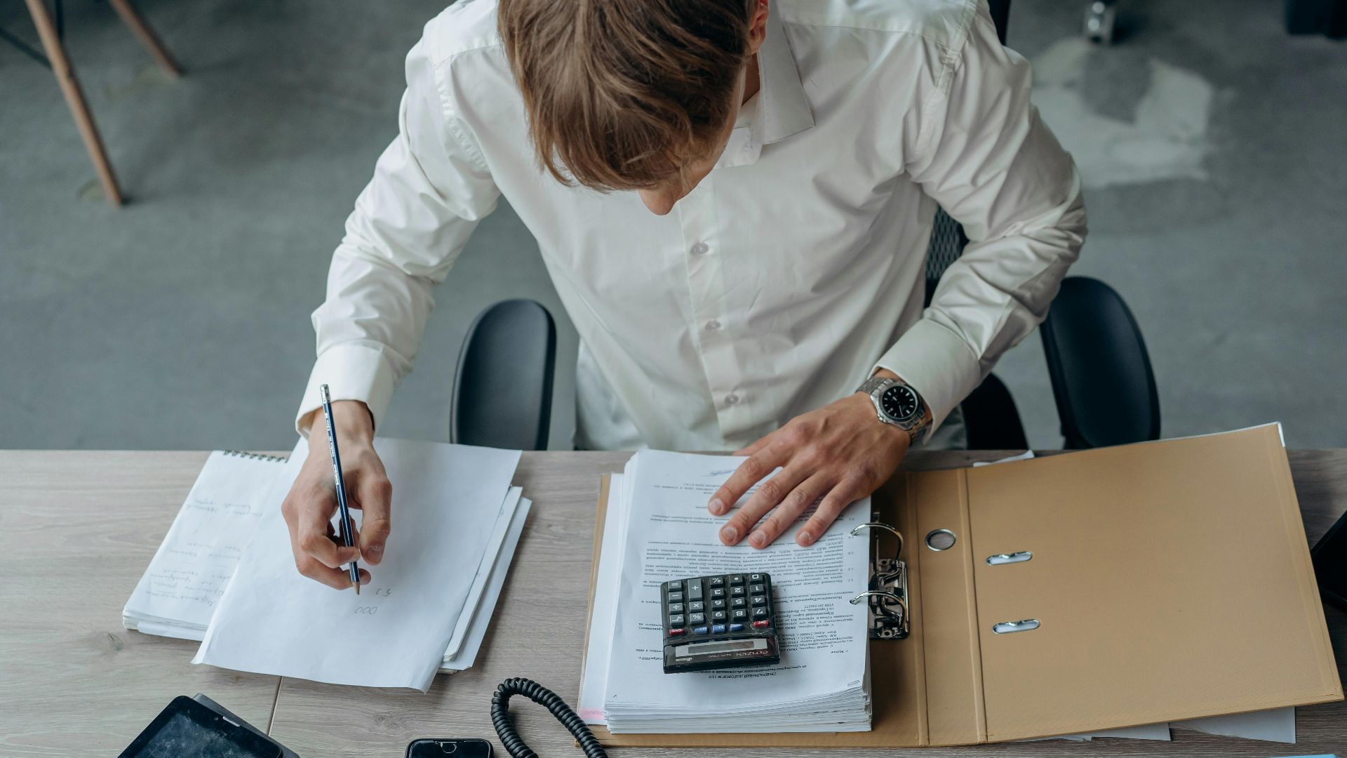 Man in an office reviewing financial papers with a calculator on a desk.