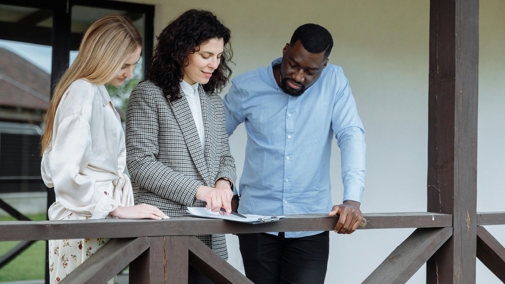 Real estate agent discussing property paperwork with a couple on a porch.