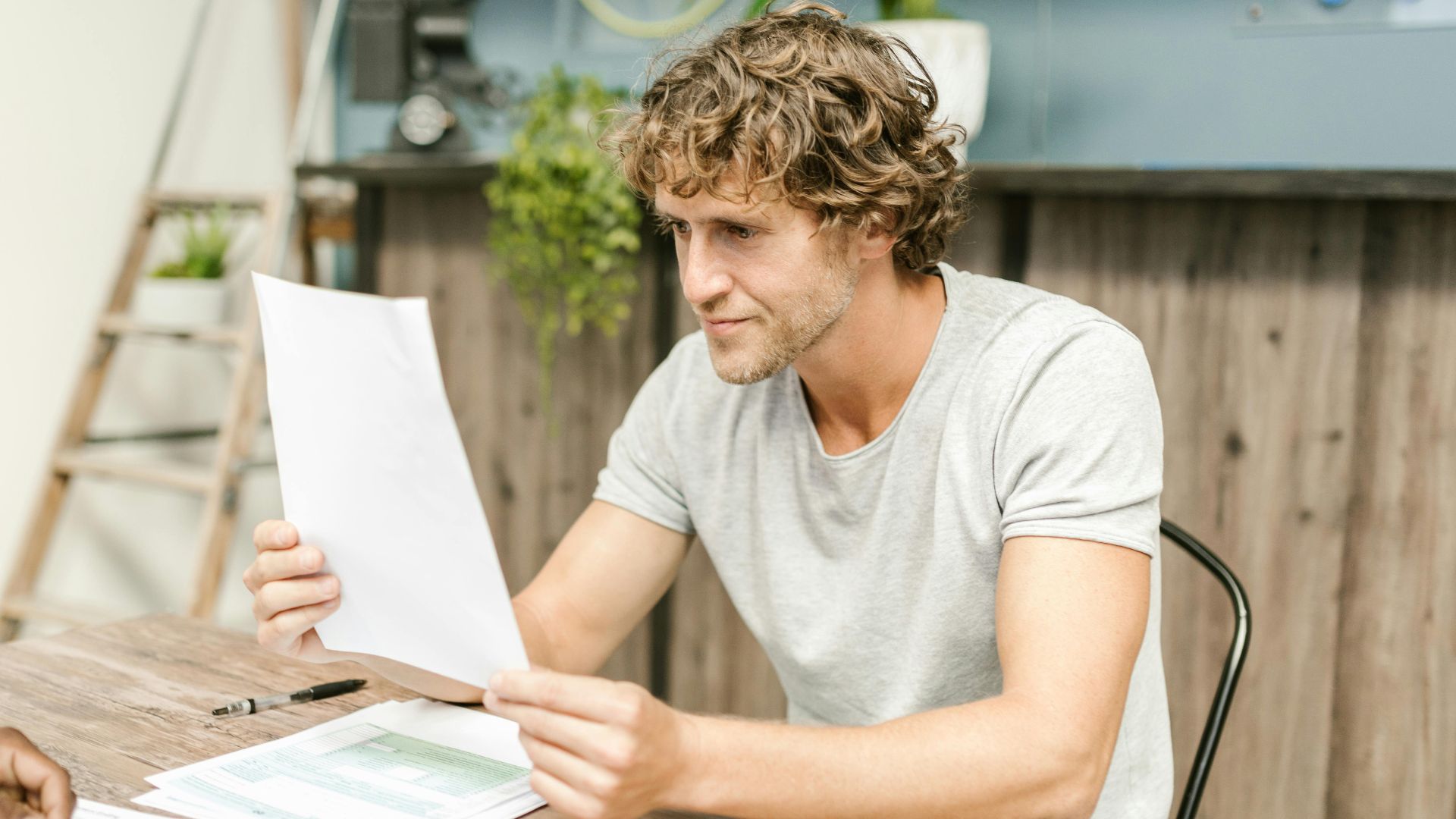 A man with curly hair evaluates documents at a desk, highlighting focused work in a professional setting.