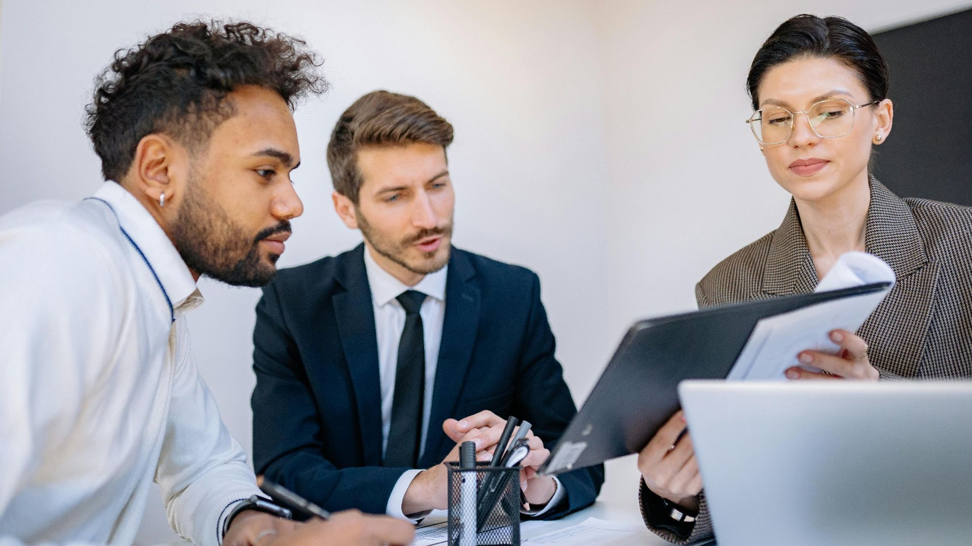 Three business professionals engaged in a focused office meeting, discussing documents.