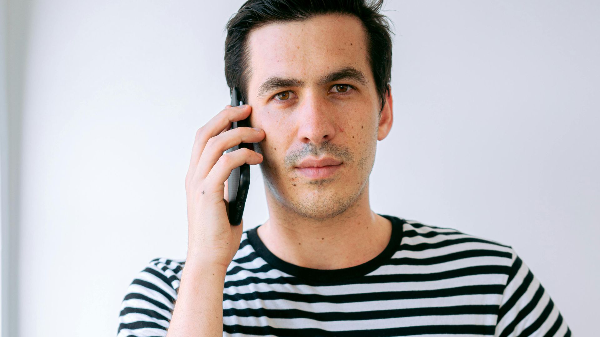 Portrait of a man in a striped shirt talking on his phone indoors.