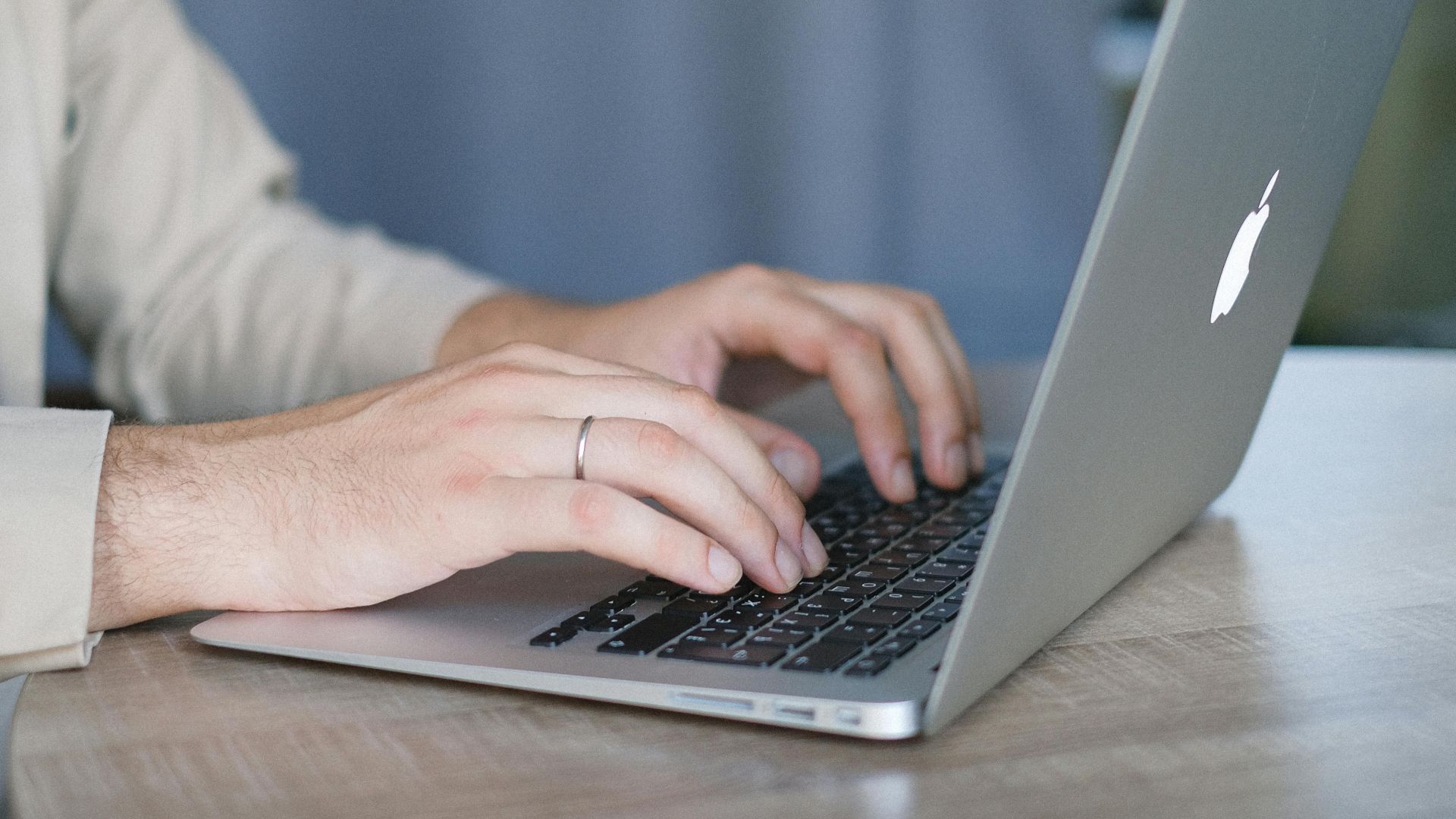 Side view of crop bearded male entrepreneur wearing classy jacket sitting at wooden table and browsing modern netbook in daylight