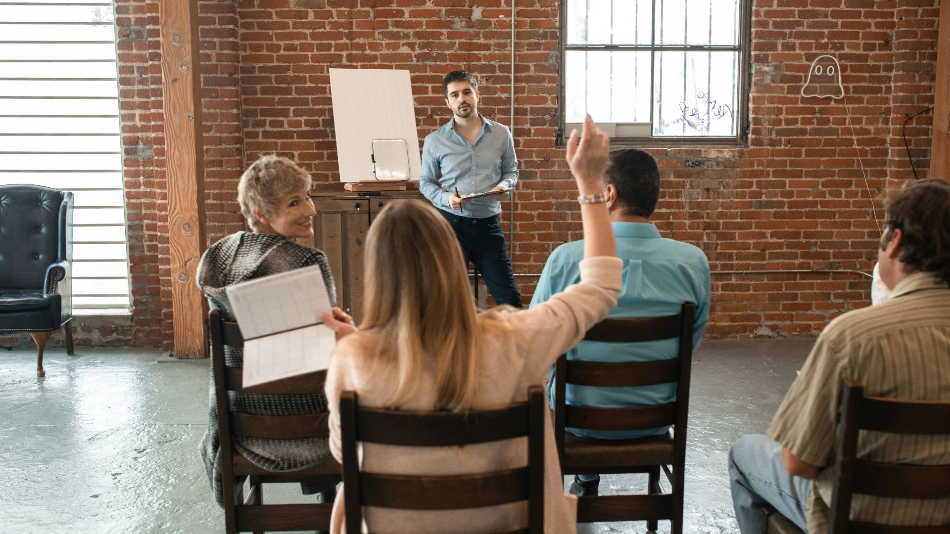 Informal meeting with diverse adults discussing topics in a brick-walled room.