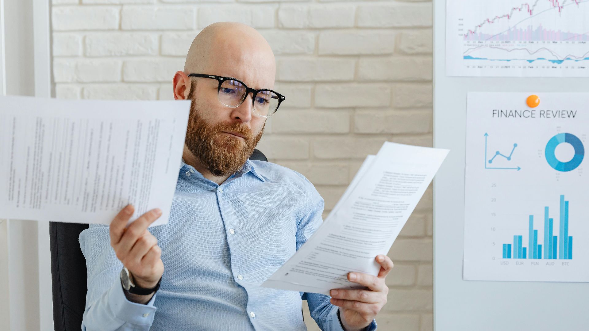 Bald bearded businessman reading financial documents in modern office setting.