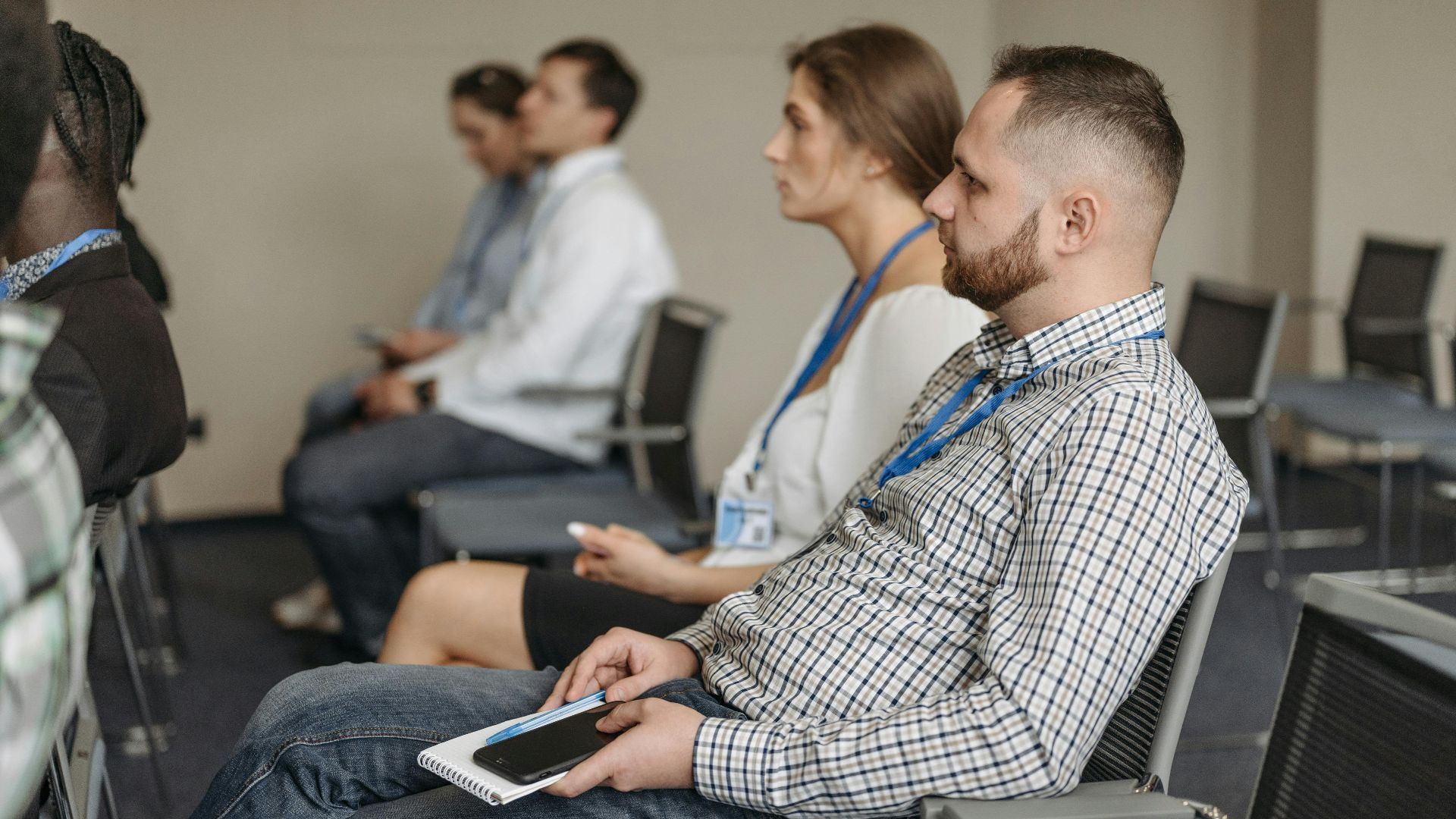 Adults attending a business seminar, attentively listening with notebooks and smartphones.