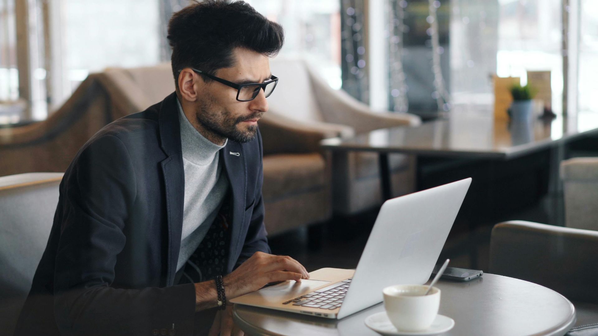Focused businessman working on a laptop in a stylish café, drinking coffee.