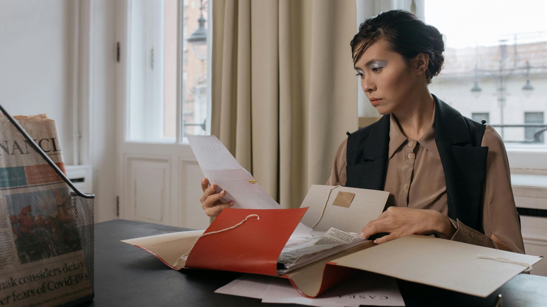 Businesswoman in an office setting reviewing important documents from a red folder with focus and determination.
