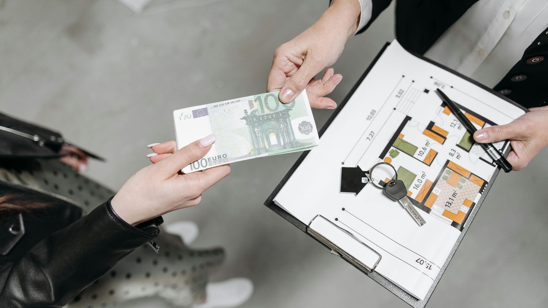 Close-up of a real estate transaction with euro bill, keys, and floor plan.